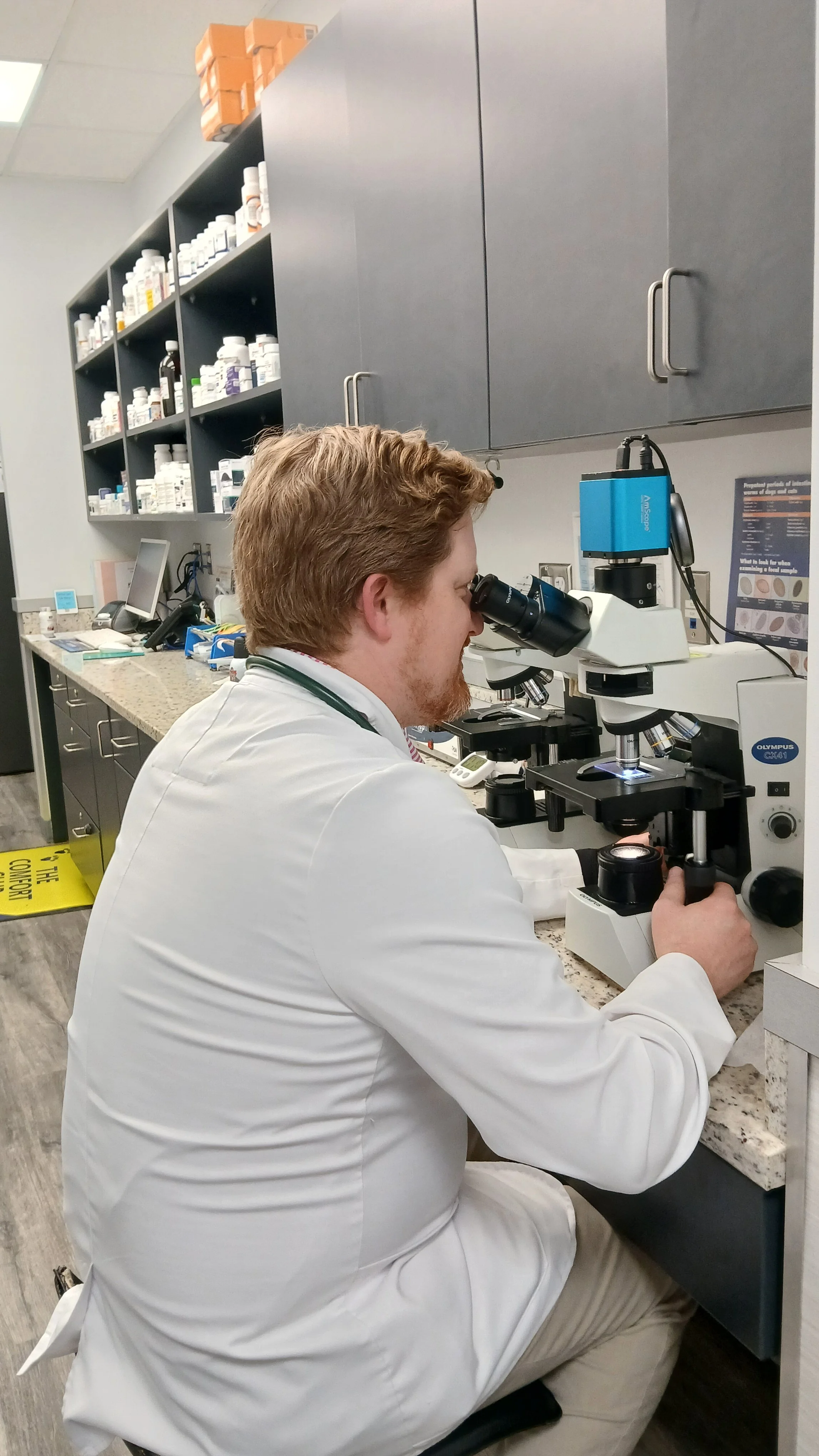 A male scientist in a white lab coat looking into a microscope in a laboratory setting.