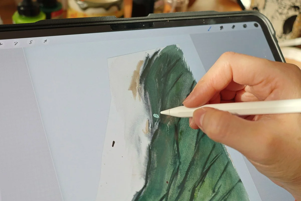 Hand using a stylus on an iPad to paint over a scanned green watercolor texture.