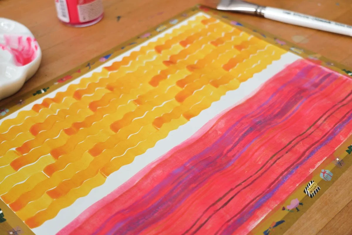 Bright yellow and pink wavy stripe pattern painted on taped paper, with palette and brush just off to the side.