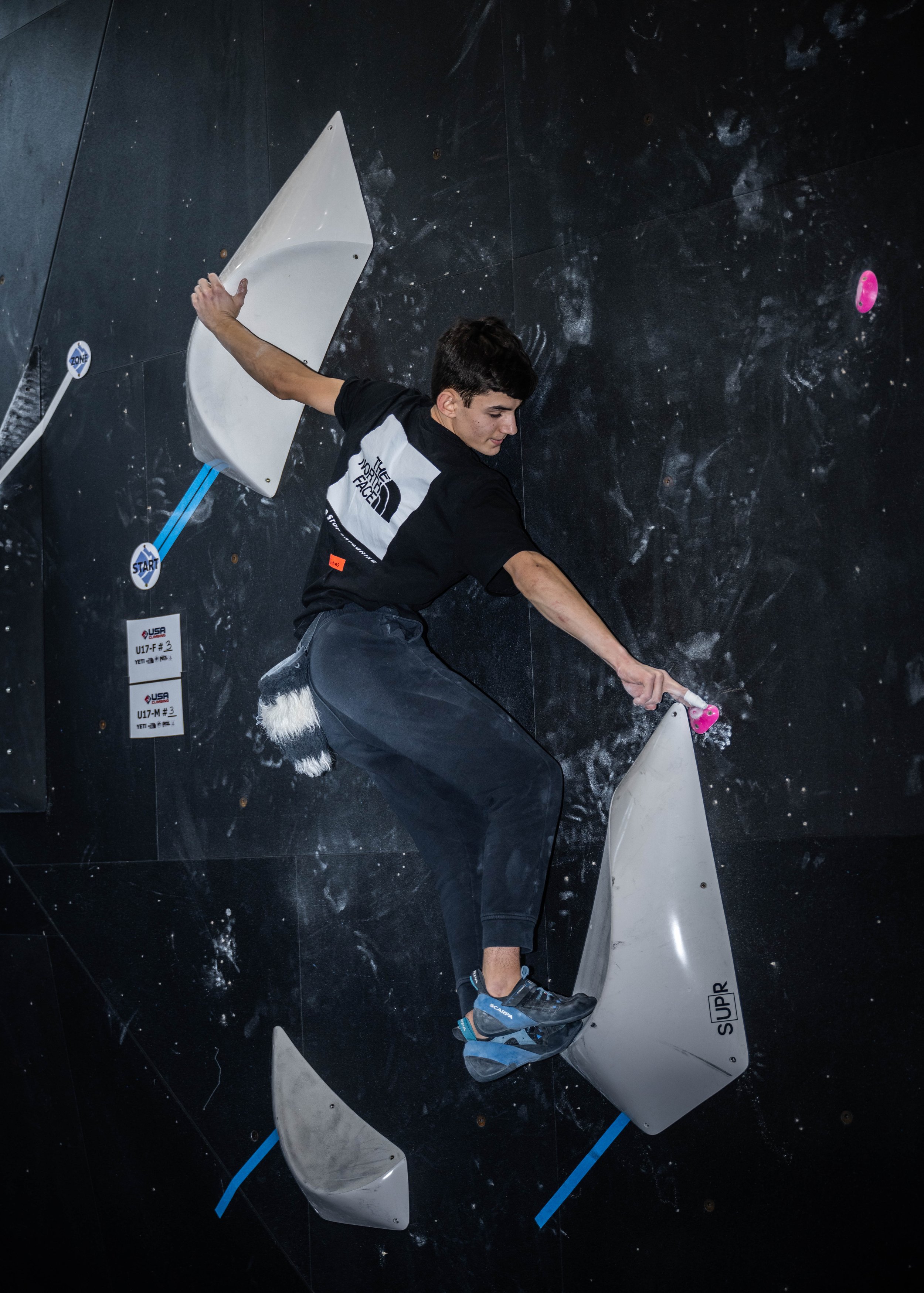 A climber on an indoor bouldering wall during a competition.