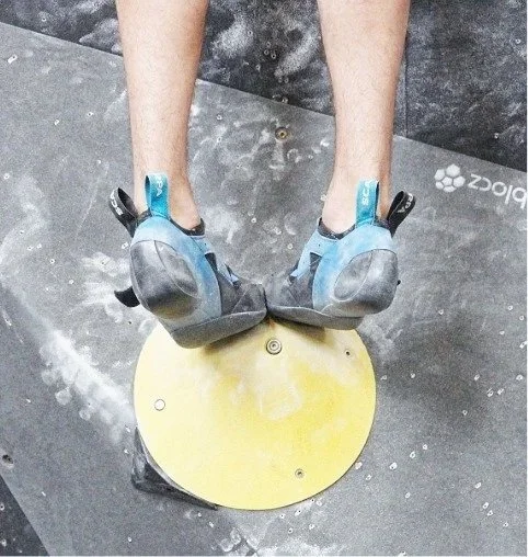 Person in climbing shoes standing on a yellow chalk bucket at the climbing gym. Indoor rock climbing.