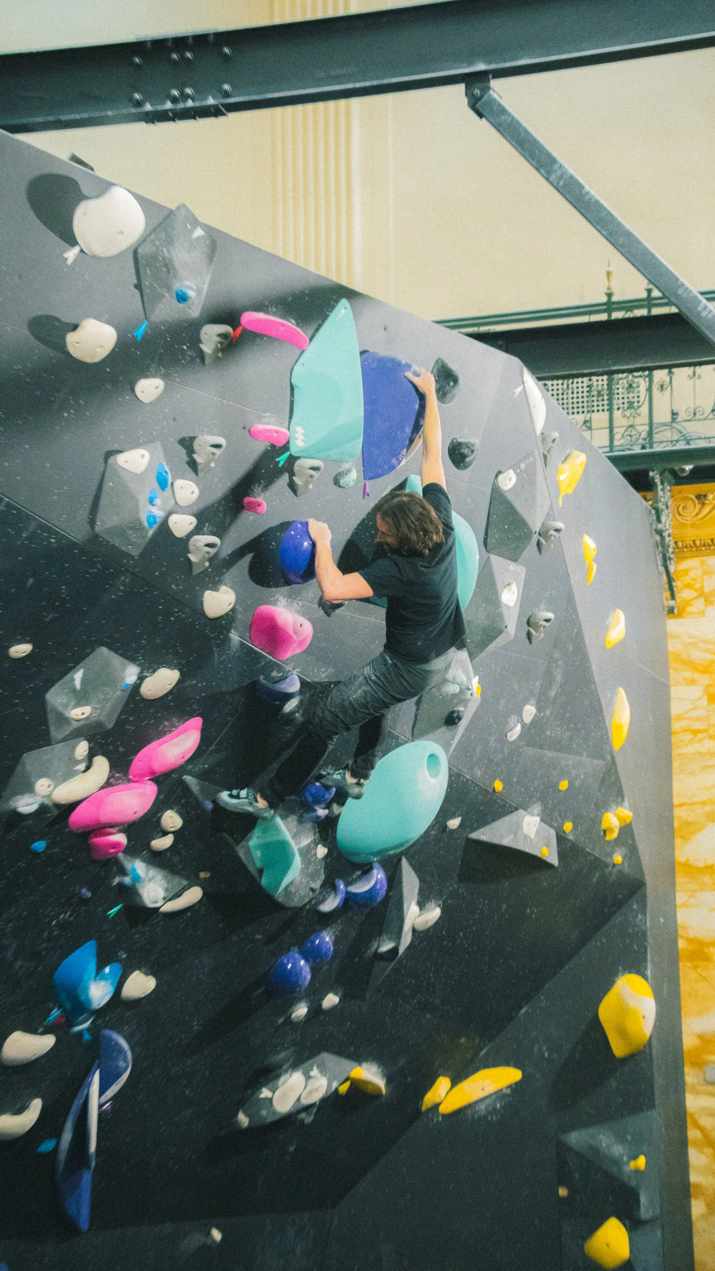 A person climbing an indoor bouldering wall with various colorful holds. Indoor rock climbing.