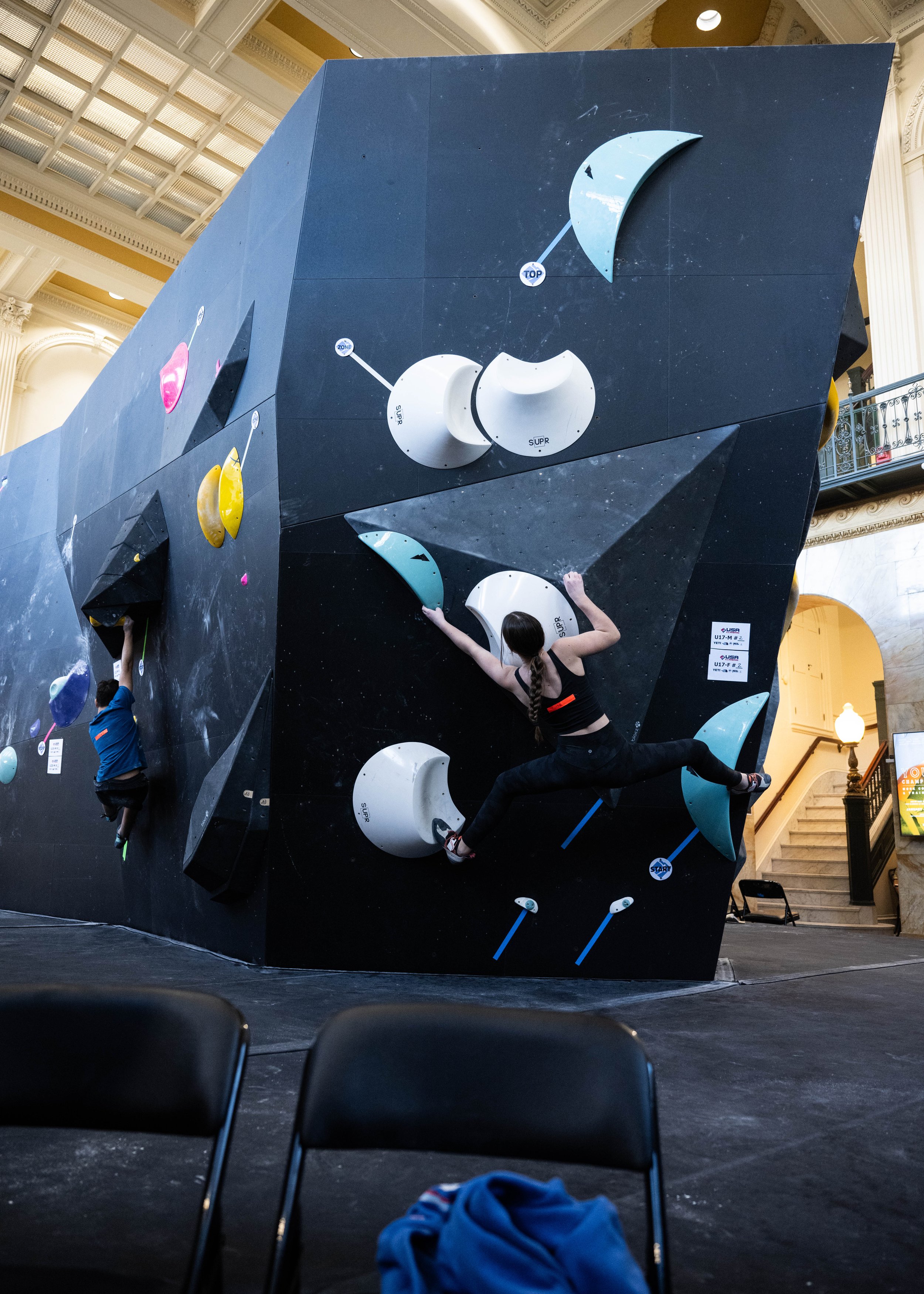 Two climbers ascending an indoor bouldering wall with colorful holds in a gym setting.