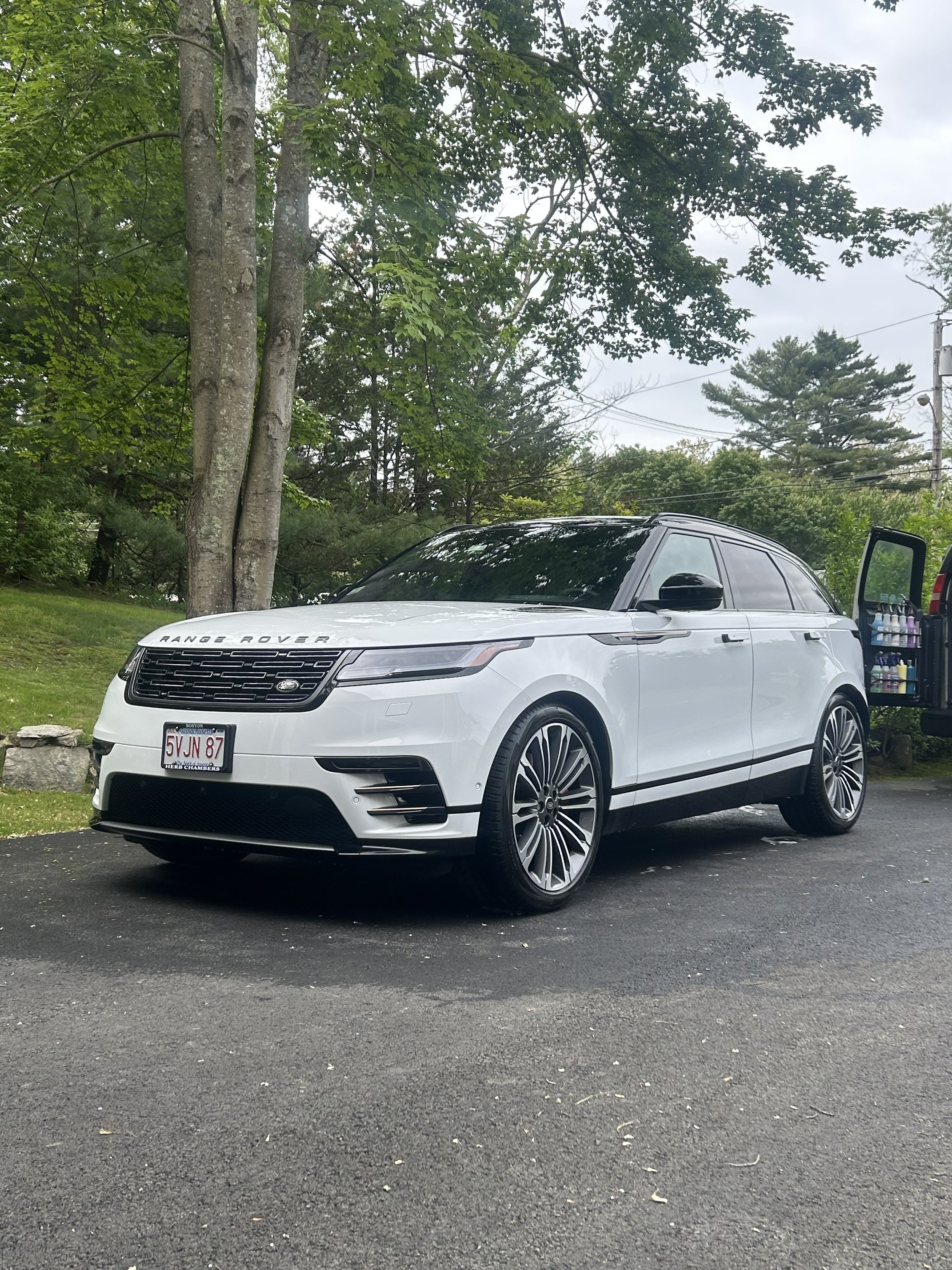 White Range Rover SUV parked on asphalt near green trees with a drink and snack cooler visible in the open rear door.