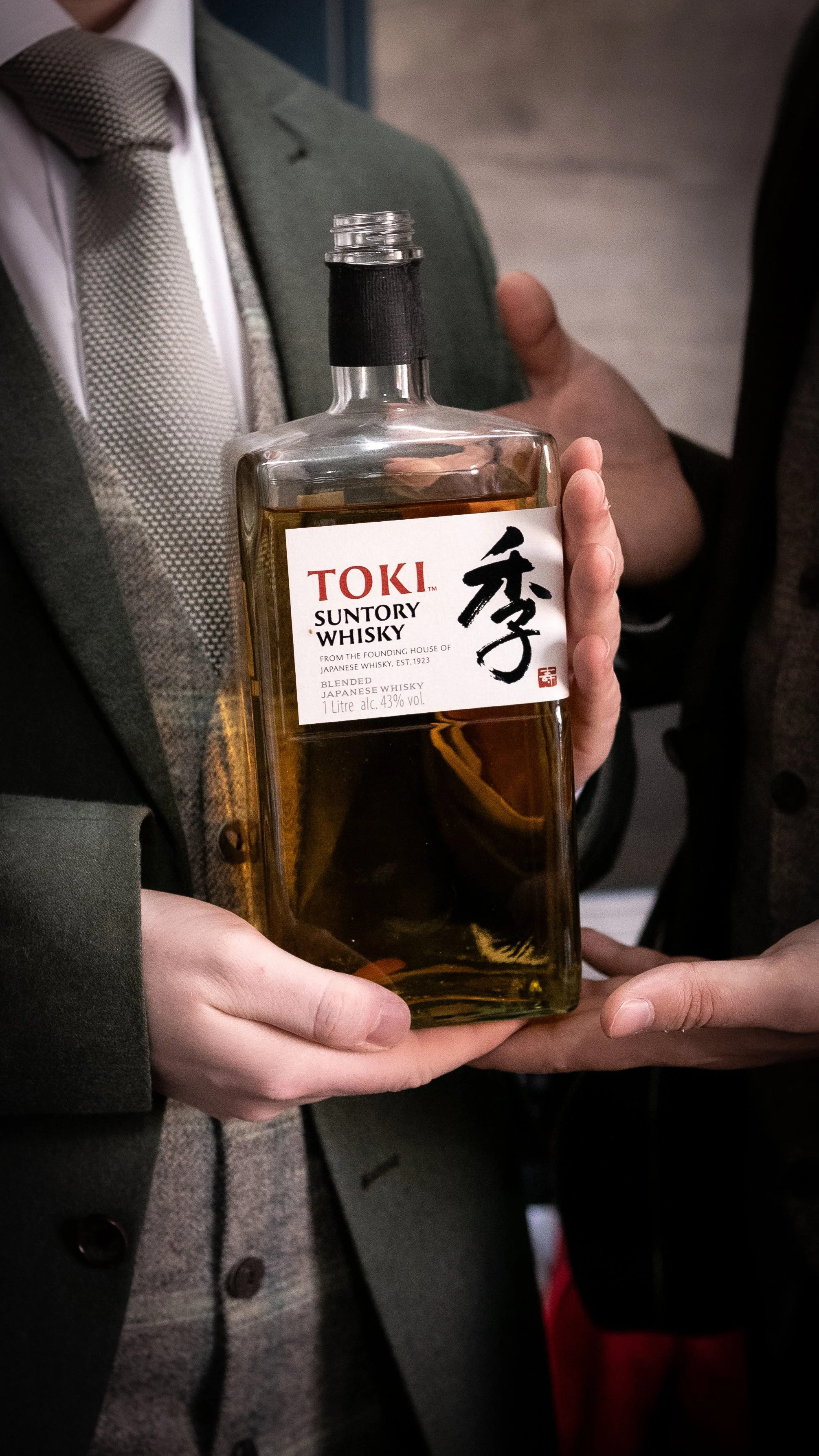 A person in formal attire holding a bottle of TOKI Suntory Whisky.