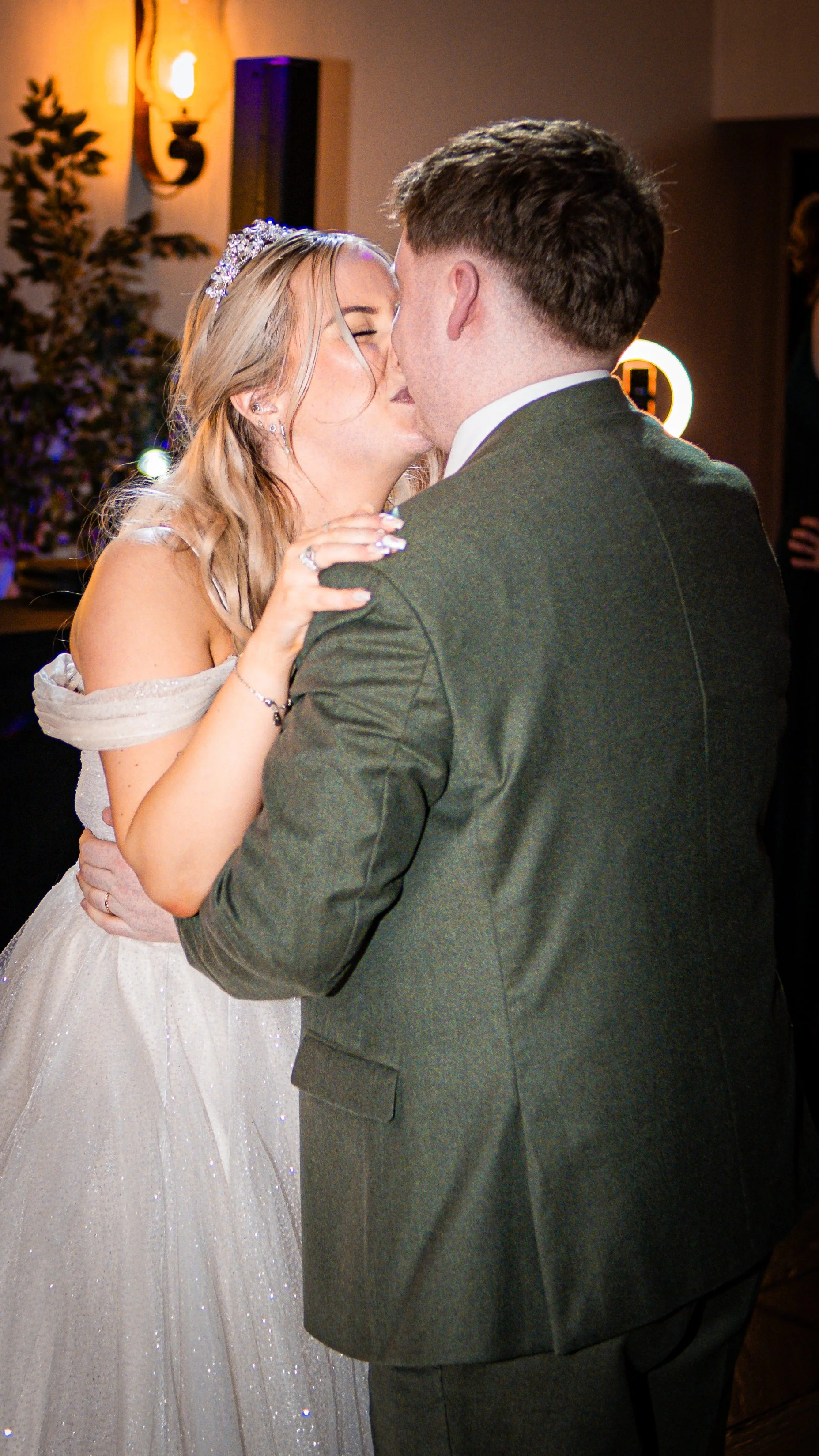 A bride and groom are dancing closely during their wedding reception, with warm lighting and wooden decor in the background.
