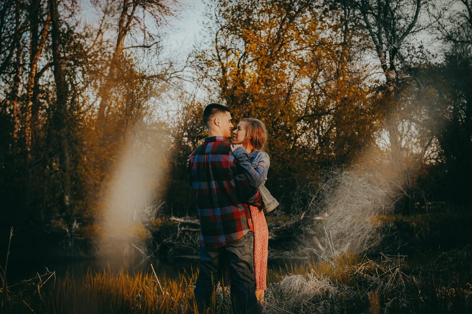 Couple embracing outdoors during fall, with trees and sunlight in background