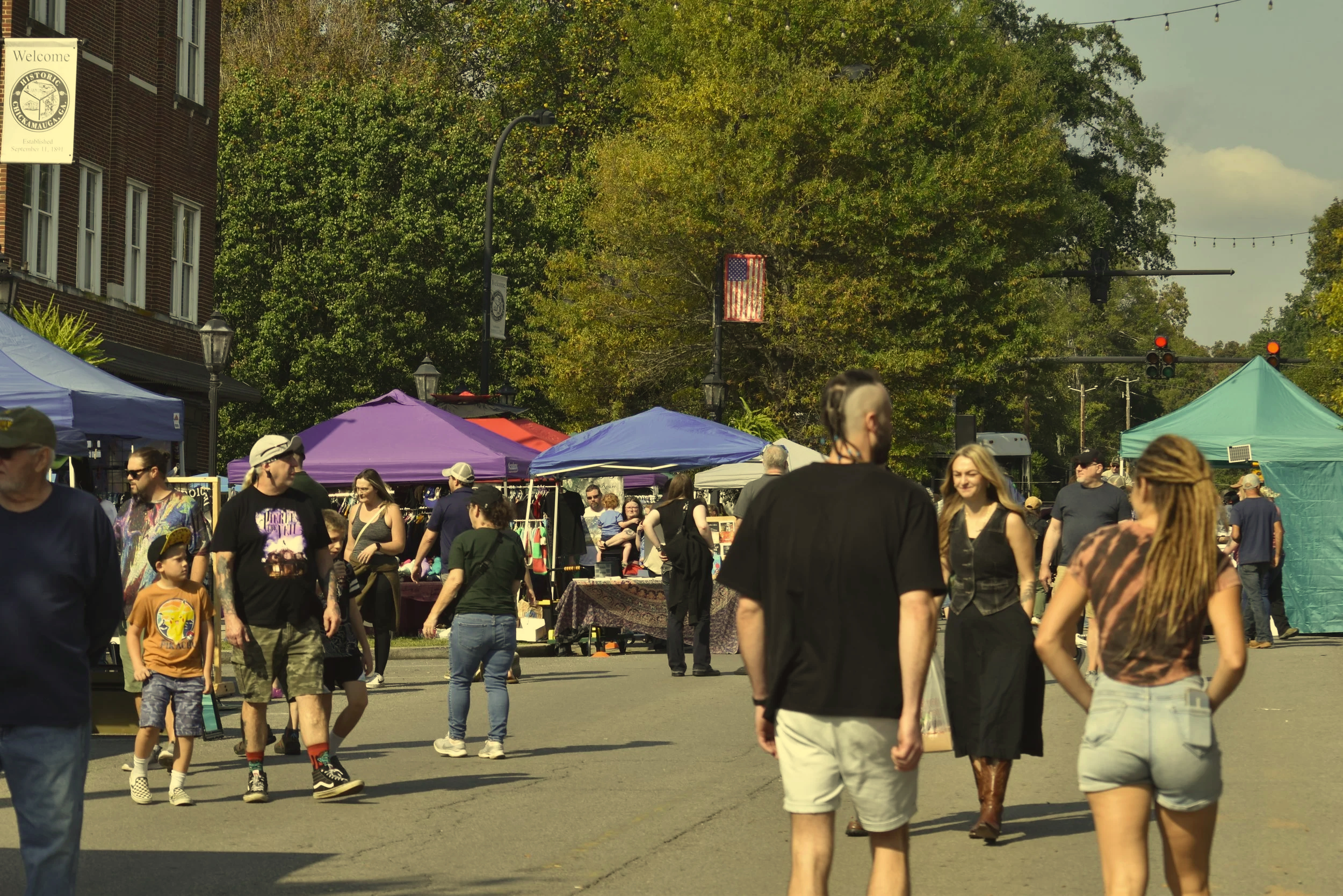Crowds explore vendor booths at the 2025 Green Eyes Festival in downtown Chickamauga, Georgia, during a sunny fall day with colorful tents, autumn trees, and local festival activities.
