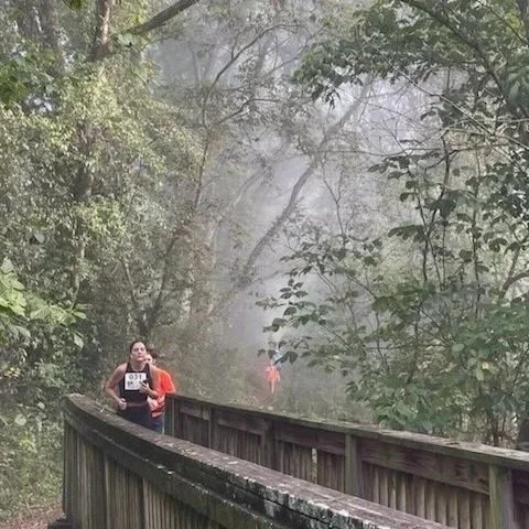 A woman running on a wooden trail surrounded by trees and fog.