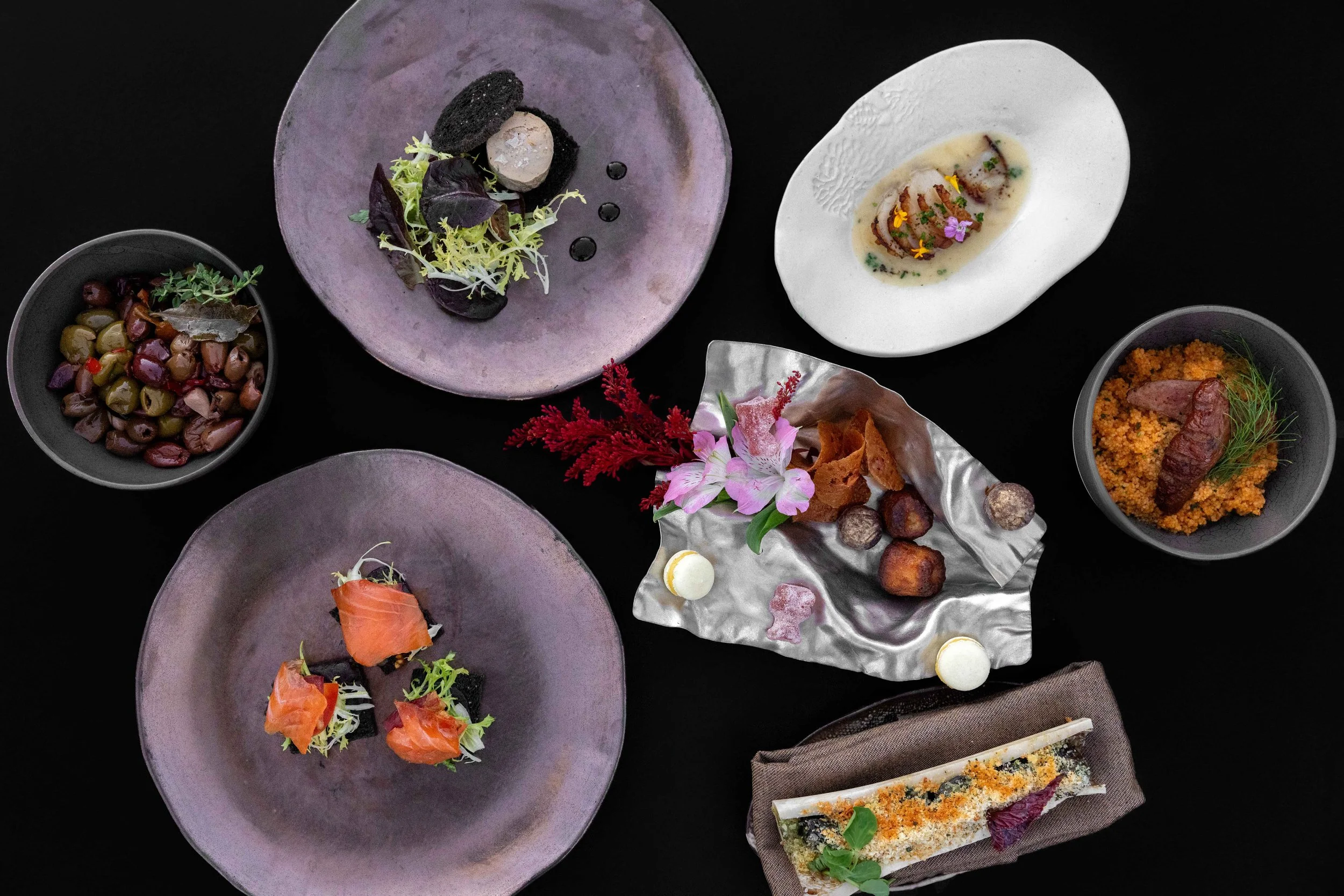 A variety Petit Plates served at Christopher's on ceramic plates and bowls, including salads, seafood, and a sandwich, with a dark background.