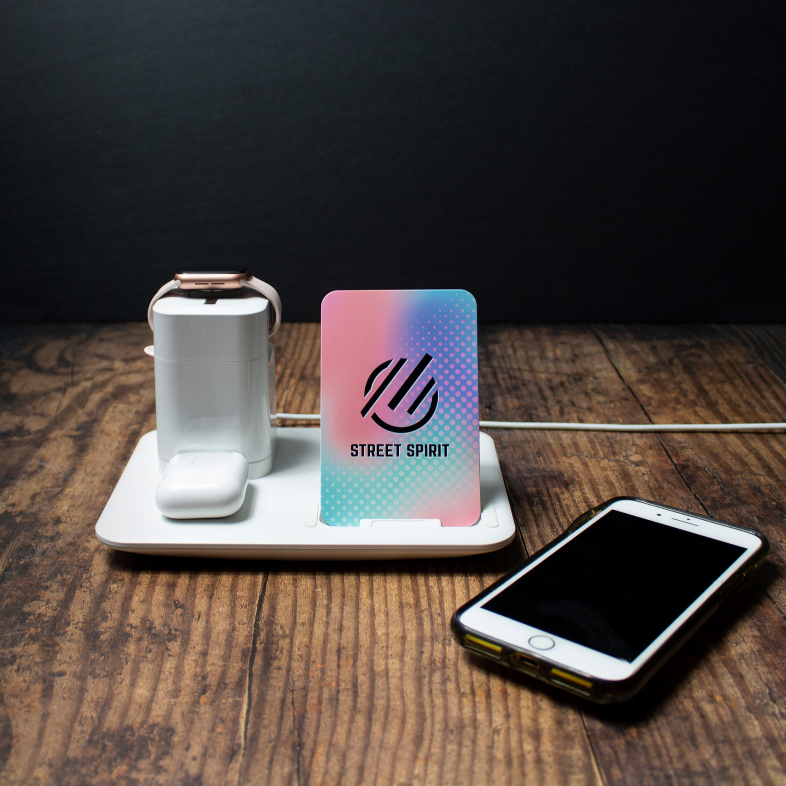 A white smartwatch with a black screen, a smartphone with a black screen and white border, a colorful card labeled 'Street Spirit' with a pink, blue, and purple gradient, and a colorful card with a pink and blue gradient and dotted pattern, all placed on a wooden surface against a black background.