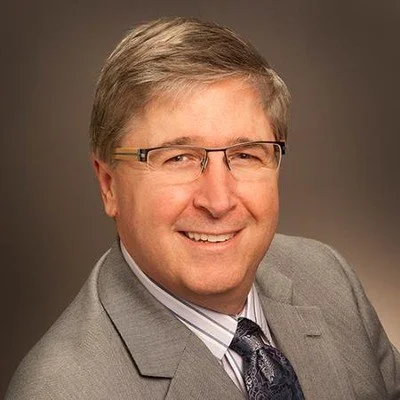 Portrait of a middle-aged man with glasses wearing a suit and tie, smiling.