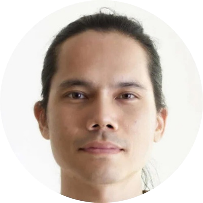 A close-up portrait of a man with dark hair pulled back, light skin, and a slight smile, against a plain white background.