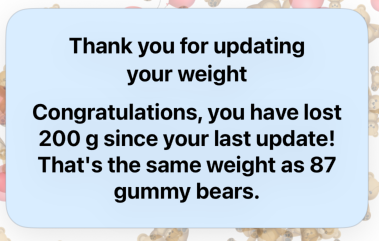 A digital notification message with a light blue background thanking for updating weight, congratulating on losing 200g since last update, and comparing the weight to 87 gummy bears.