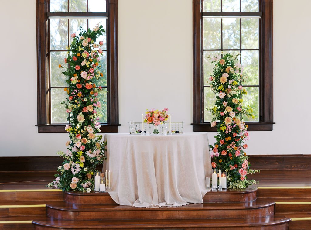 Wedding sweetheart table with peach and pink floral arrangements on two pillars, featuring a bridal bouquet in a fresh grapefruit-inspired color palette.