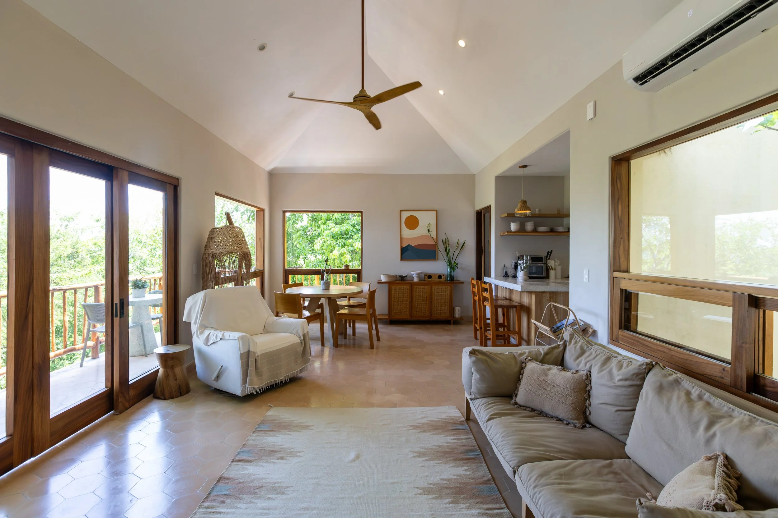 Living room with large windows, wooden dining table with chairs, beige sofa, and artwork on the wall. Perfect for family satys.