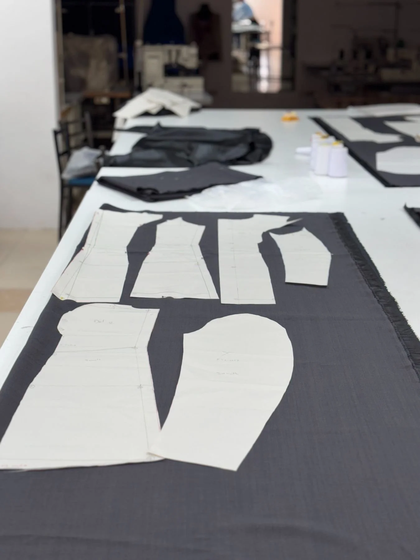 Workshop table with black fabric cutouts and patterns for a project, surrounded by sewing or craft materials.