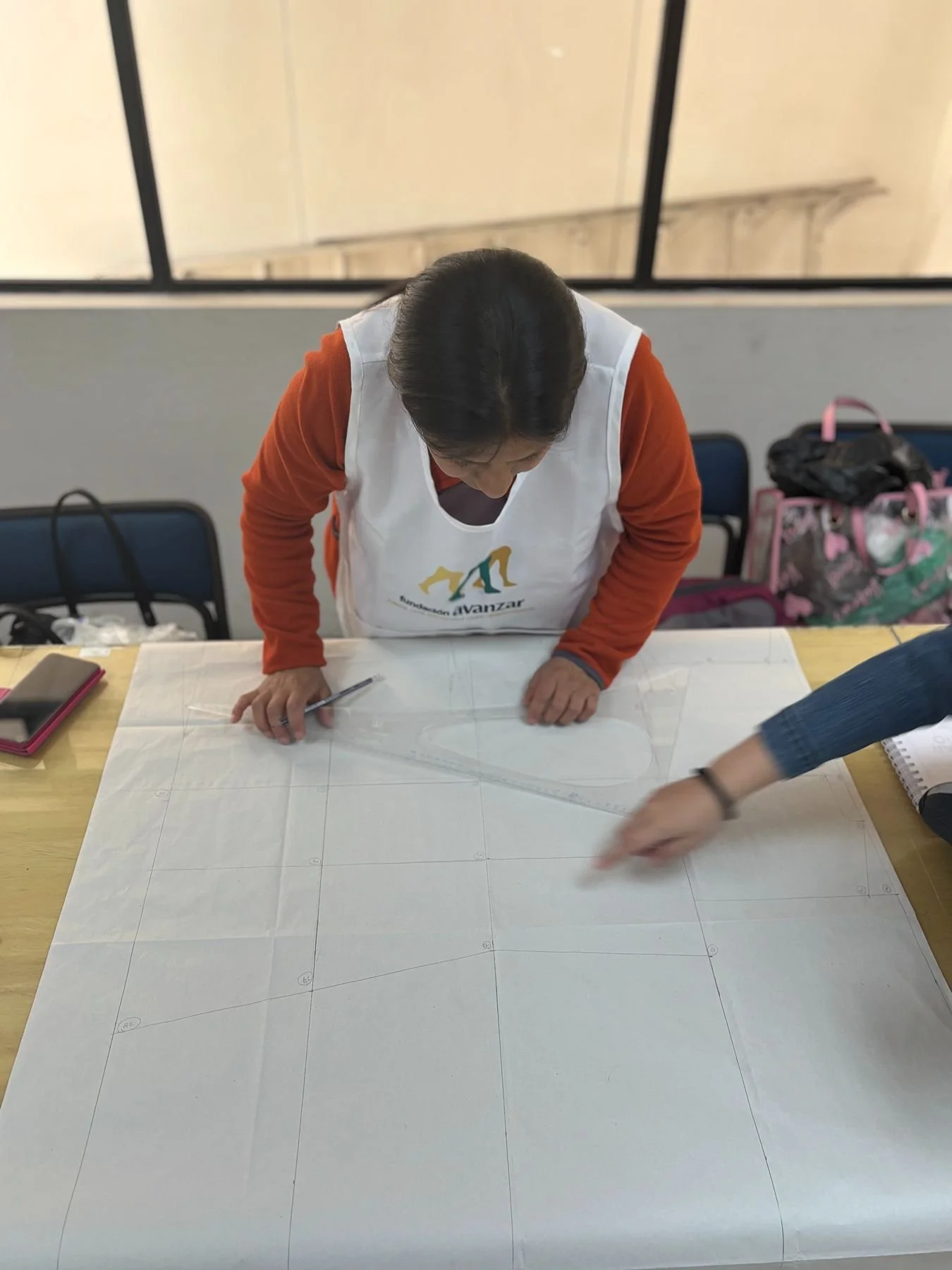 A woman in an orange long sleeve shirt and white apron is examining blueprints on a table.