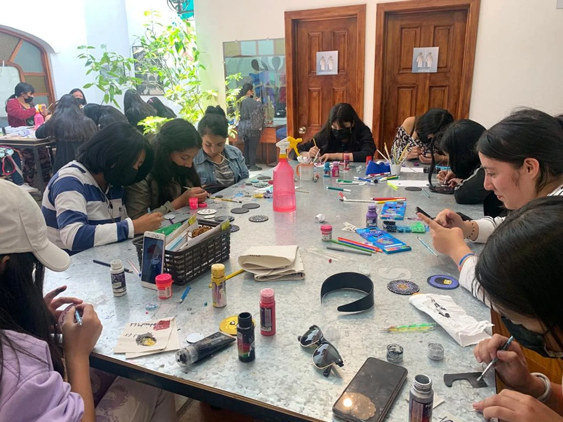 Group of people sitting around a table engaged in arts and crafts activities, with various art supplies scattered on the table.