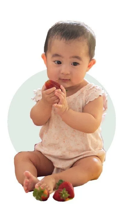 Baby sitting up holding a strawberry
