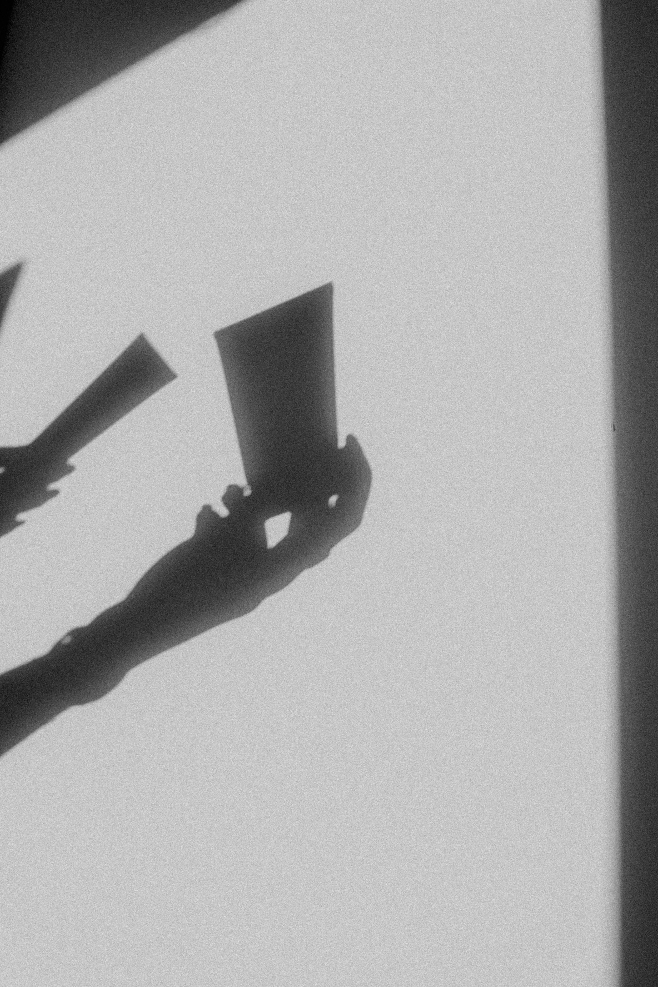 Silhouette of a person's hand holding two sheets of paper, casting shadows on a wall.