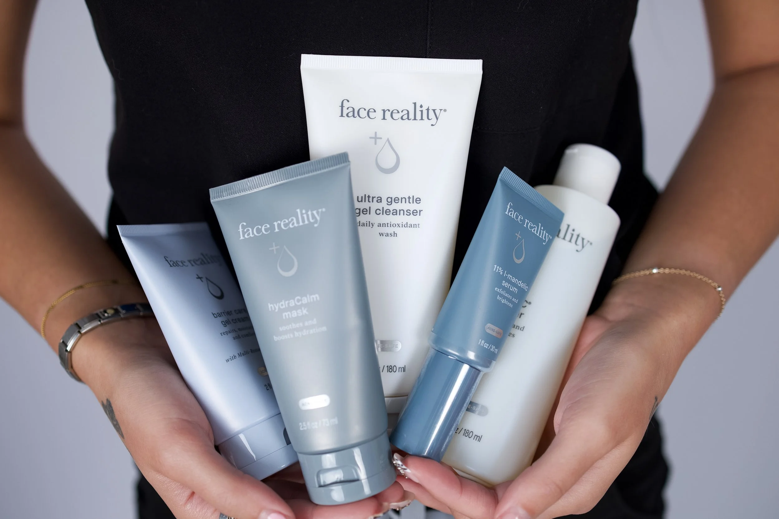 A person holding multiple skincare tubes and bottles labeled 'face reality,' with a focus on skincare products.