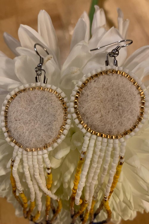 A pair of Dog fur felted disc earrings with beaded edging and fringe, displayed on a white flower with a wooden background.