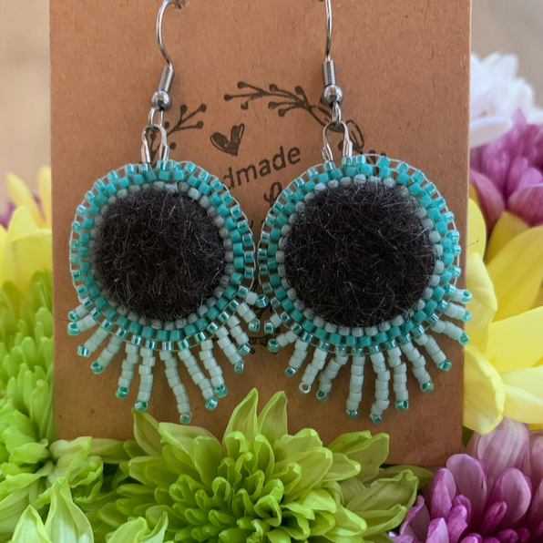 Beaded earrings with black felted centers and turquoise bead borders displayed on a brown card with floral illustrations, surrounded by yellow, green, and purple flowers.