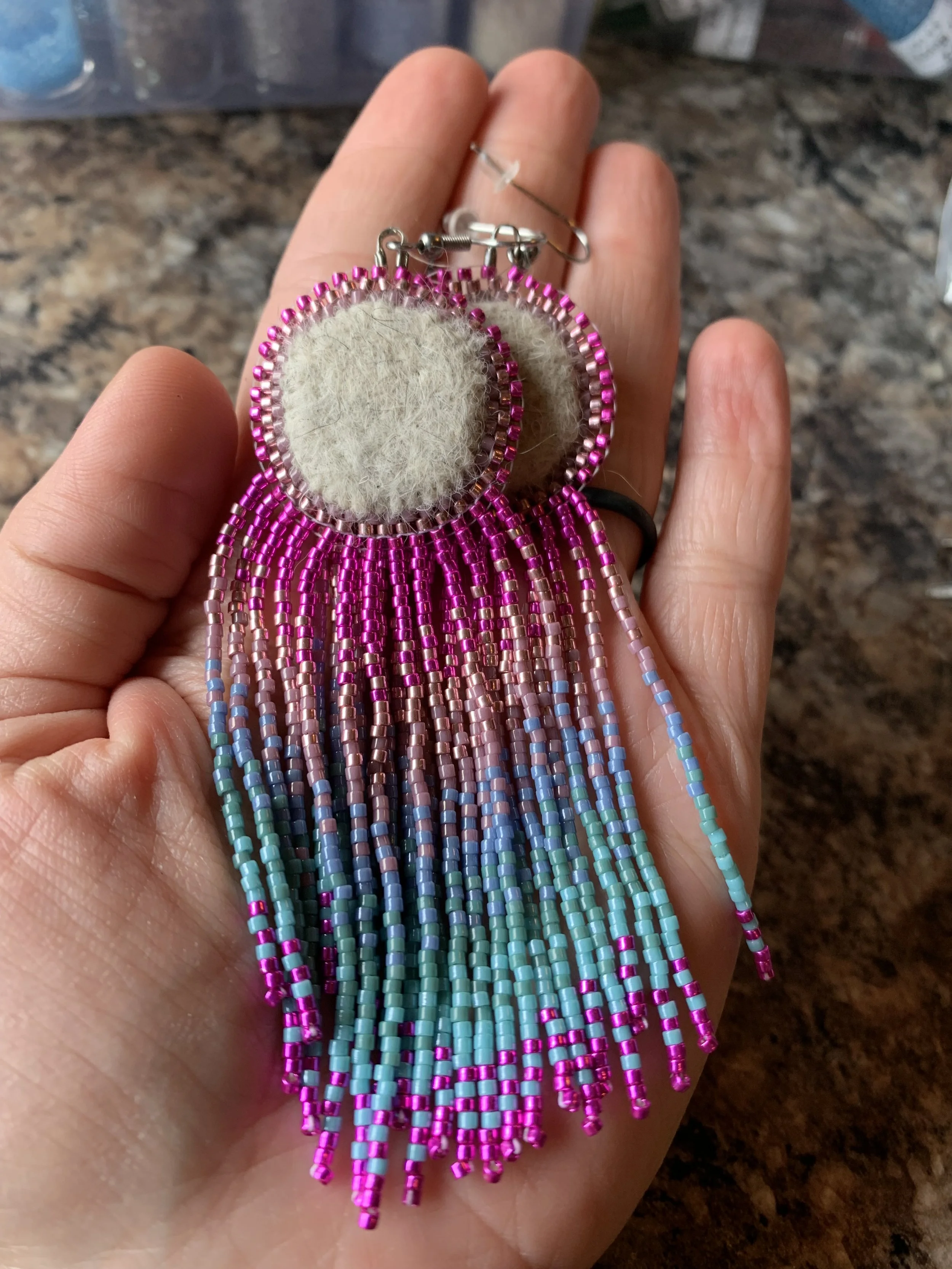 round needle felted earrings made from the undercoat of a shedding alaskan husky with shimmering pink and teal beads hanging from the felted center.