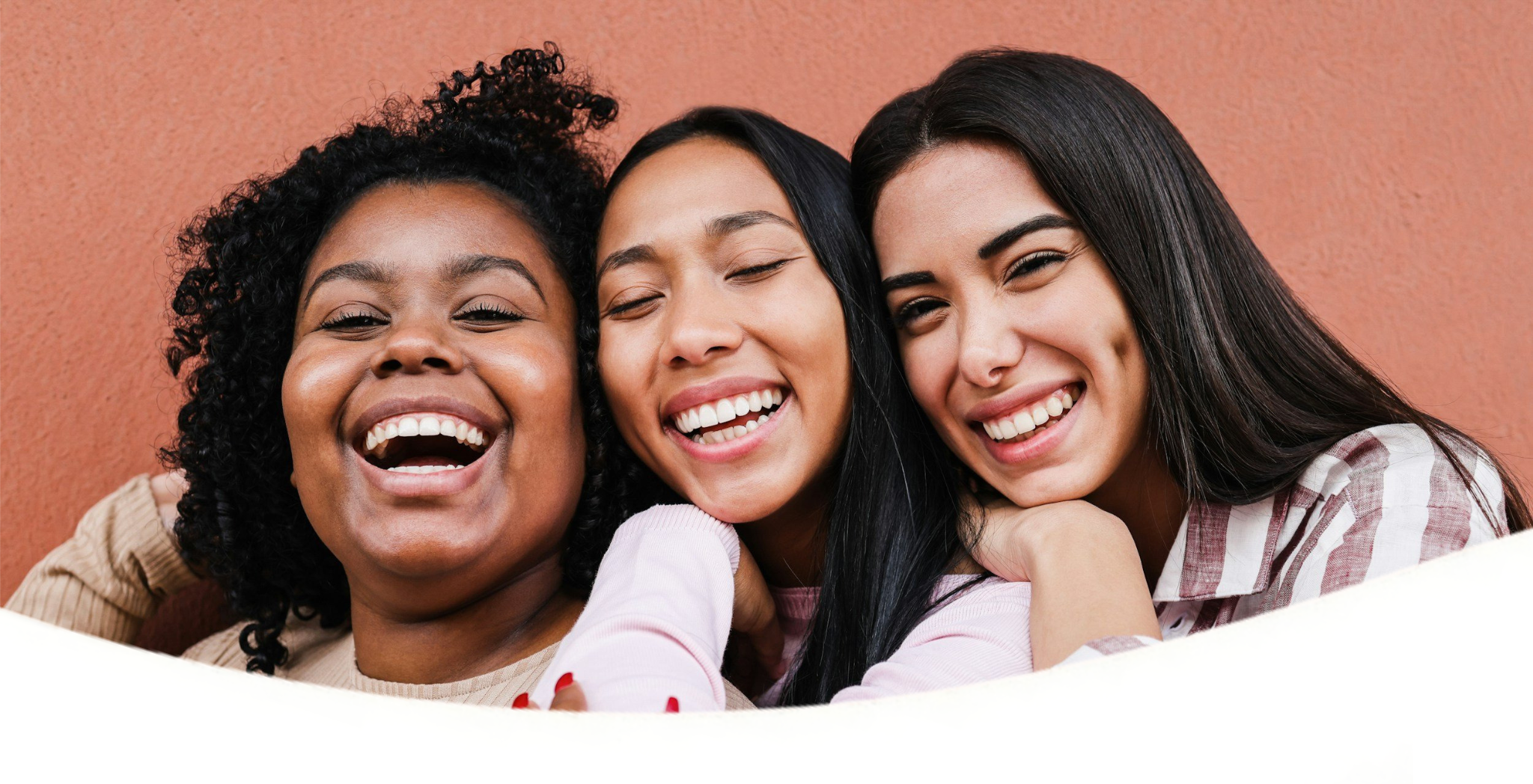 Group of diverse women smiling and hugging in a casual setting.