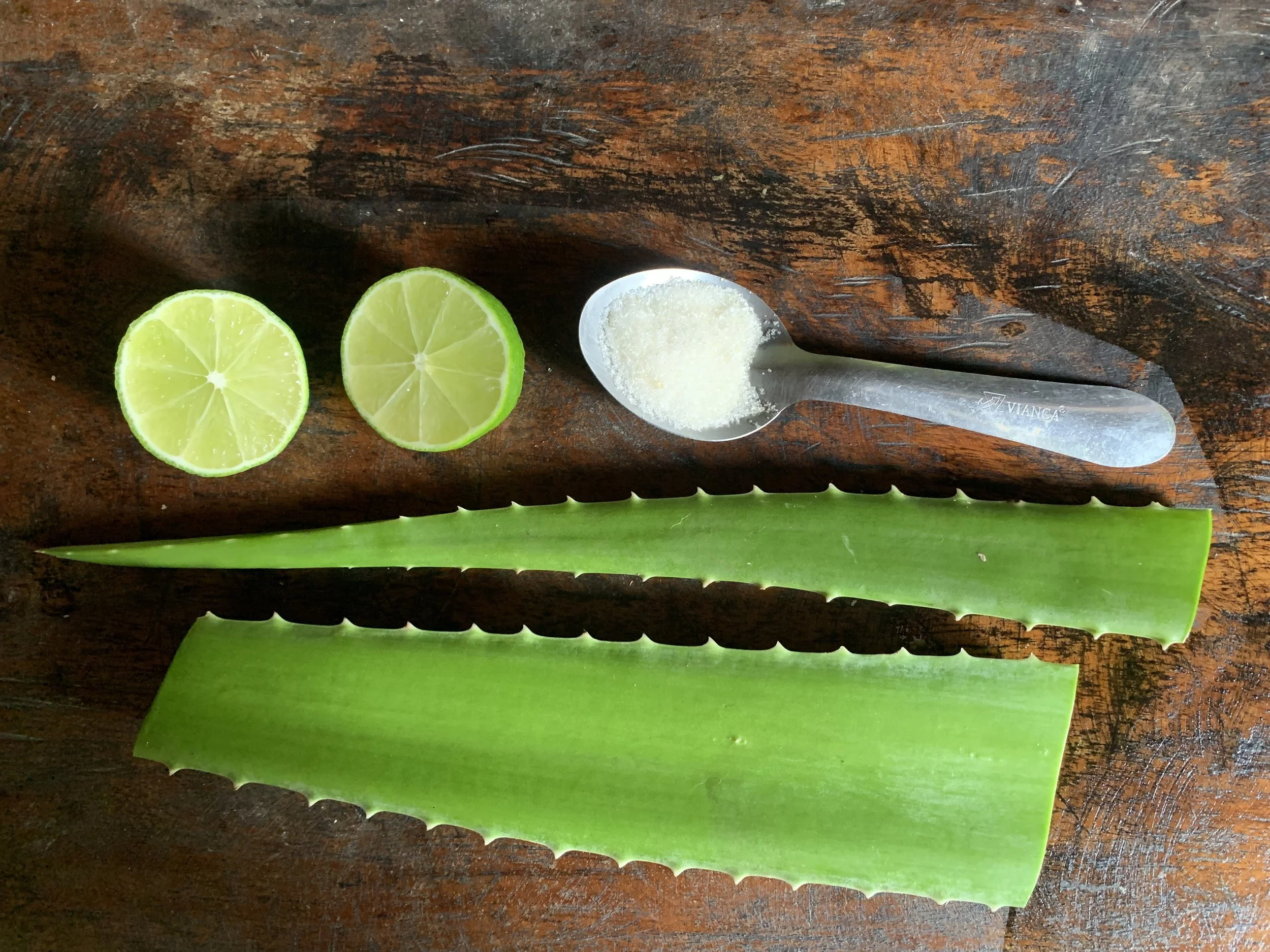 Cut aloe vera leaves, sliced lime, and a spoonful of sugar on a wooden surface
