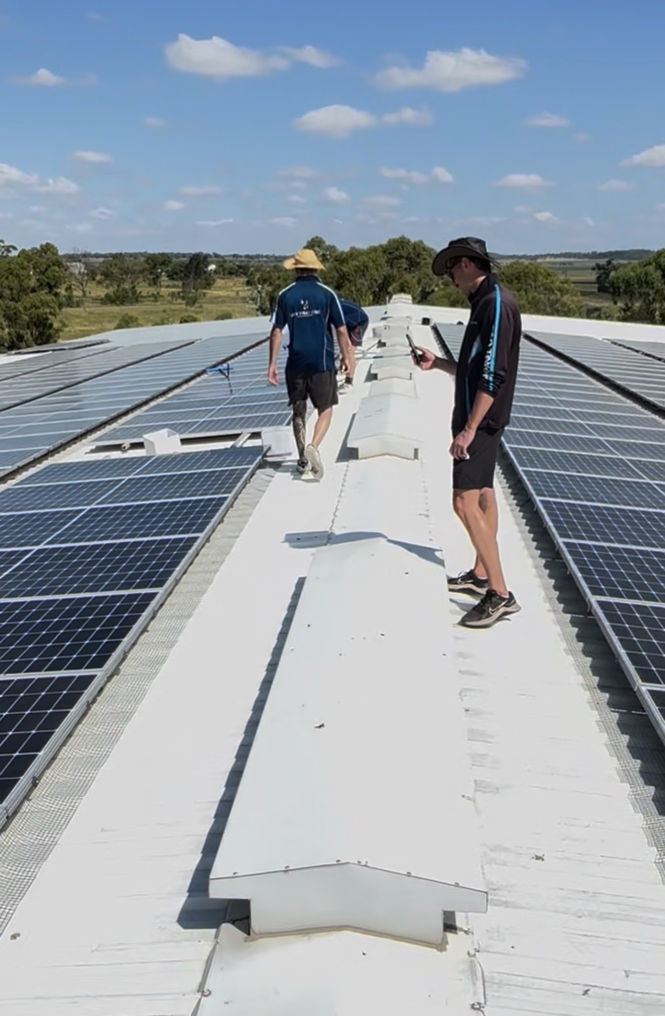 Two workers inspecting solar panels on a rooftop under a partly cloudy sky.