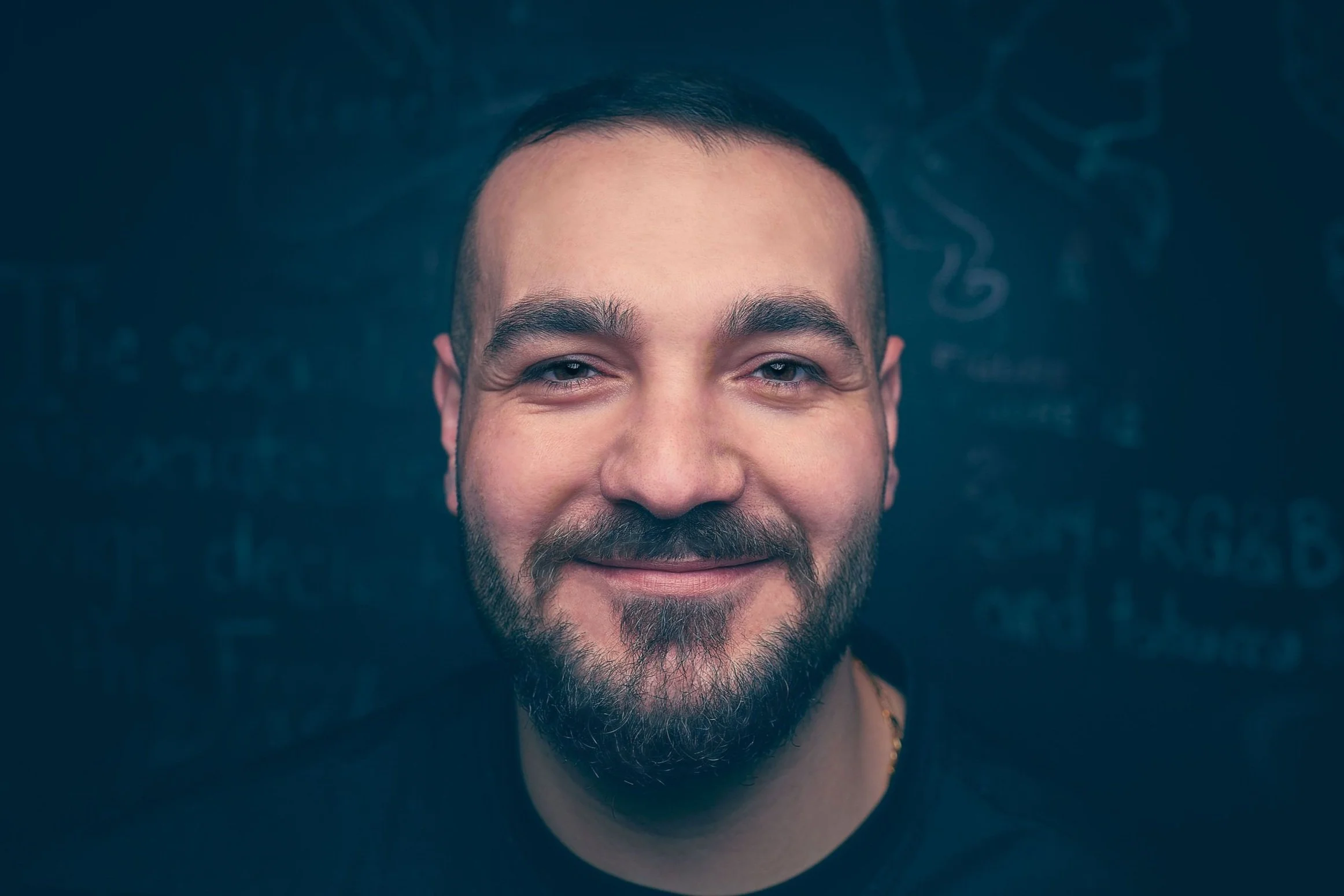 Smiling man with a beard against a dark background with chalk writing