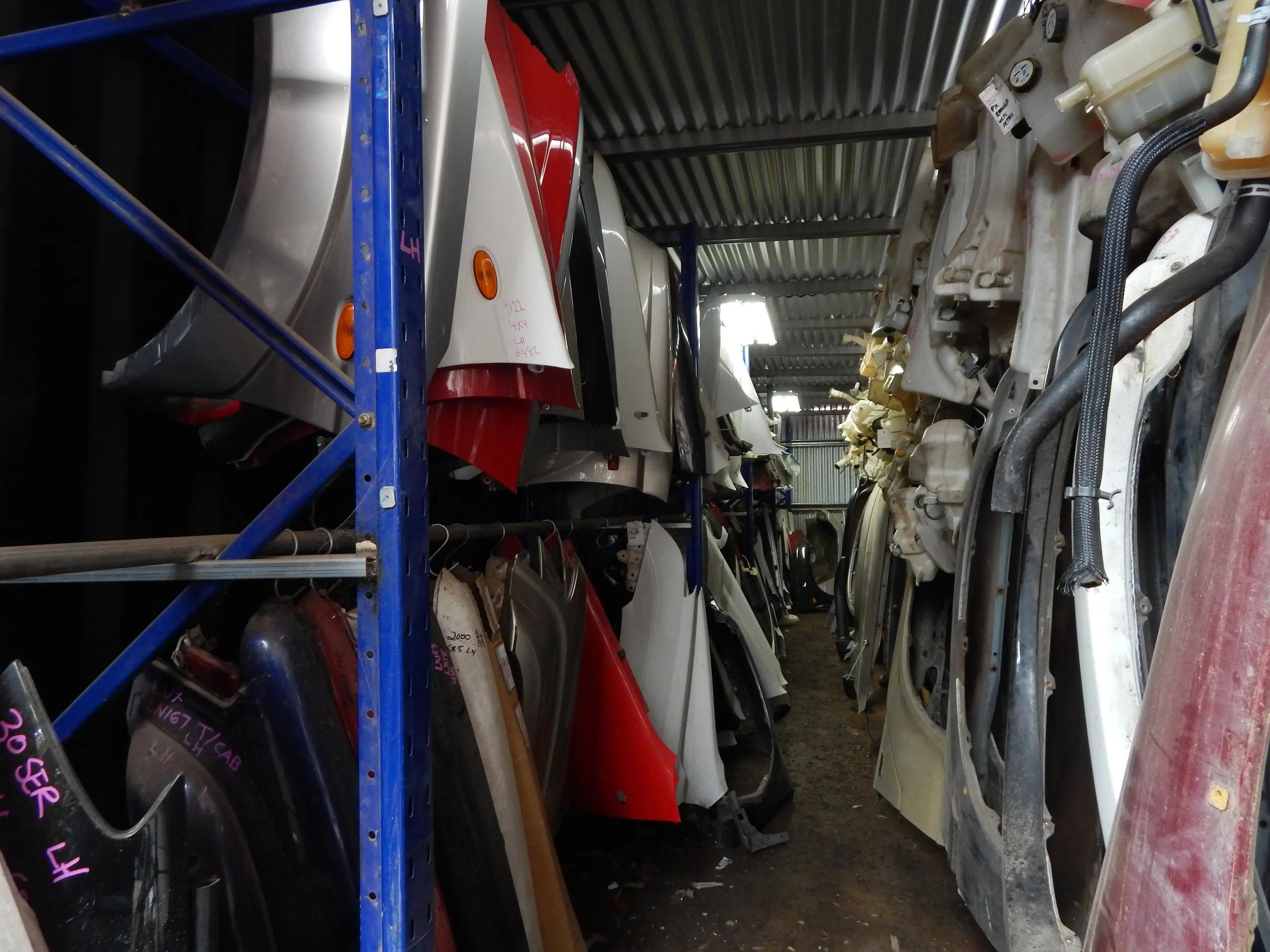 A storage area with shelves holding various car parts, including car fenders and body panels, in an industrial setting.