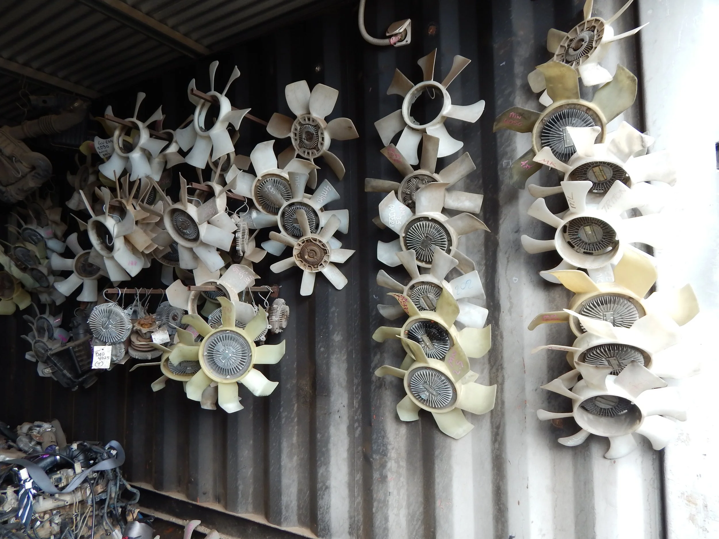 A collection of used automotive fan blades and fan assemblies hanging on a wall.
