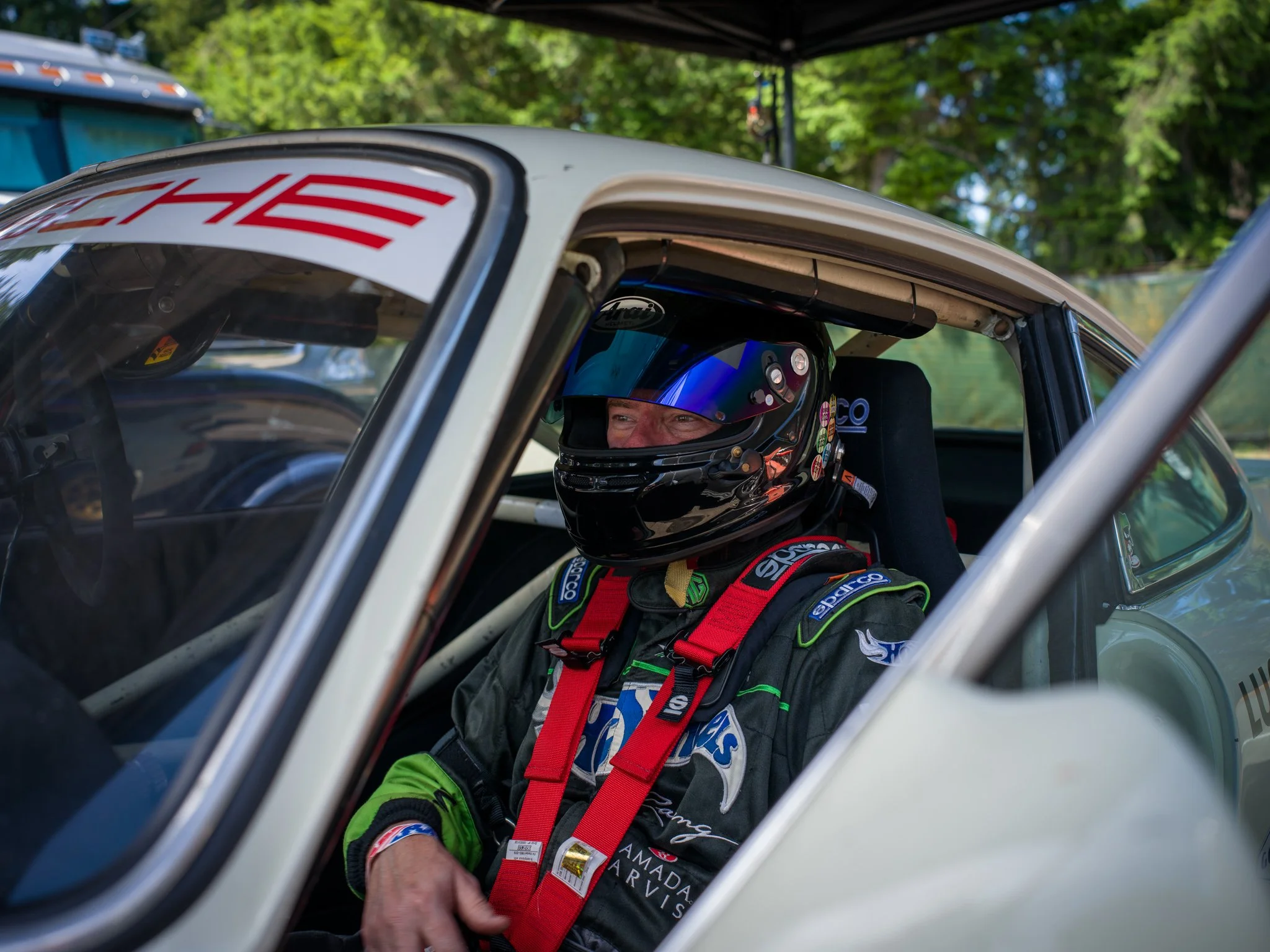 Racing driver wearing a helmet and racing suit sitting inside a race car during a race event.