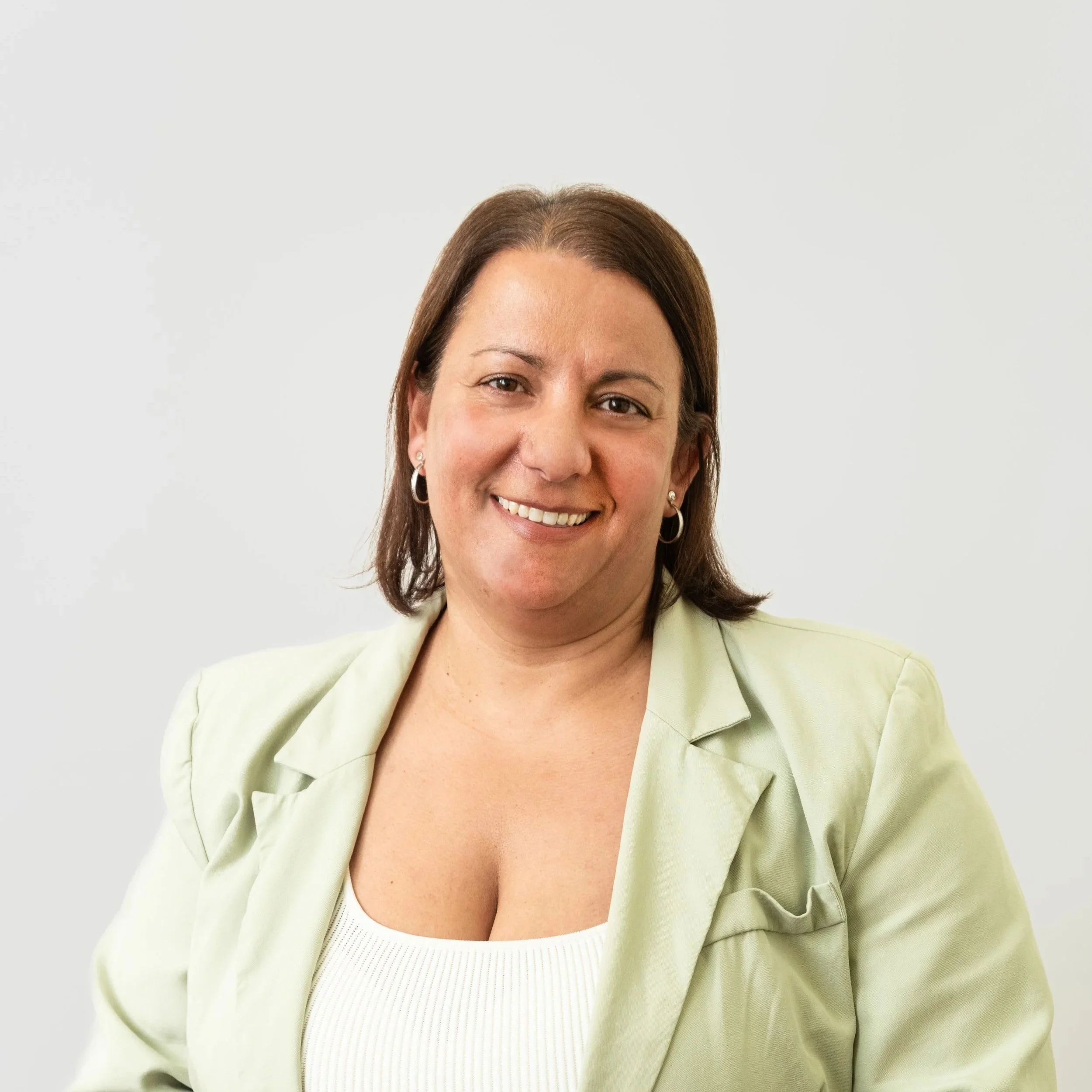 Portrait of a woman with shoulder-length dark hair, wearing a checkered shirt, earrings, and a necklace, smiling against a white background.