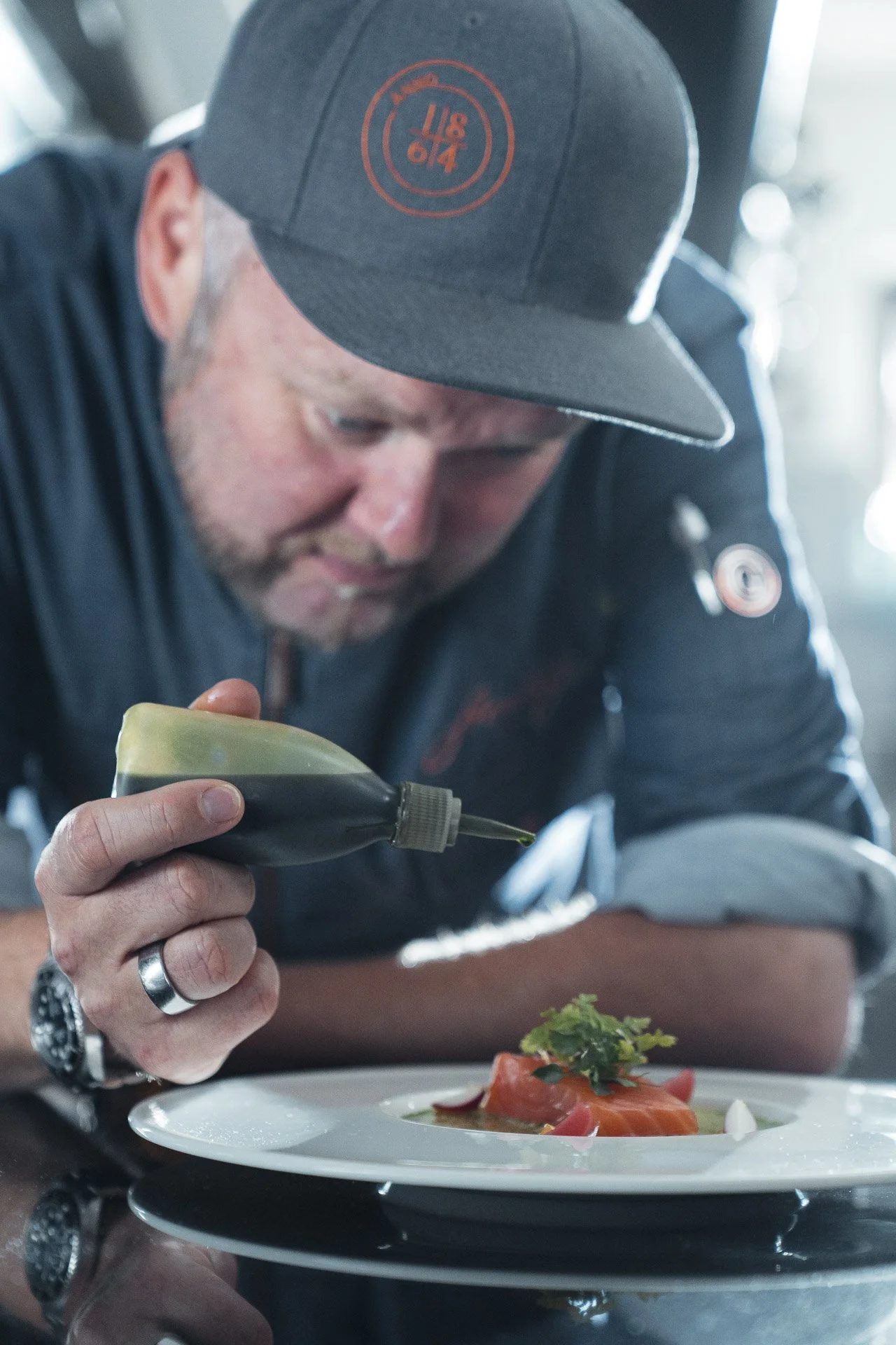 Ein Koch konzentriert sich darauf, eine Soße auf ein kunstvoll angerichtetes Gericht auf einem Teller zu träufeln.