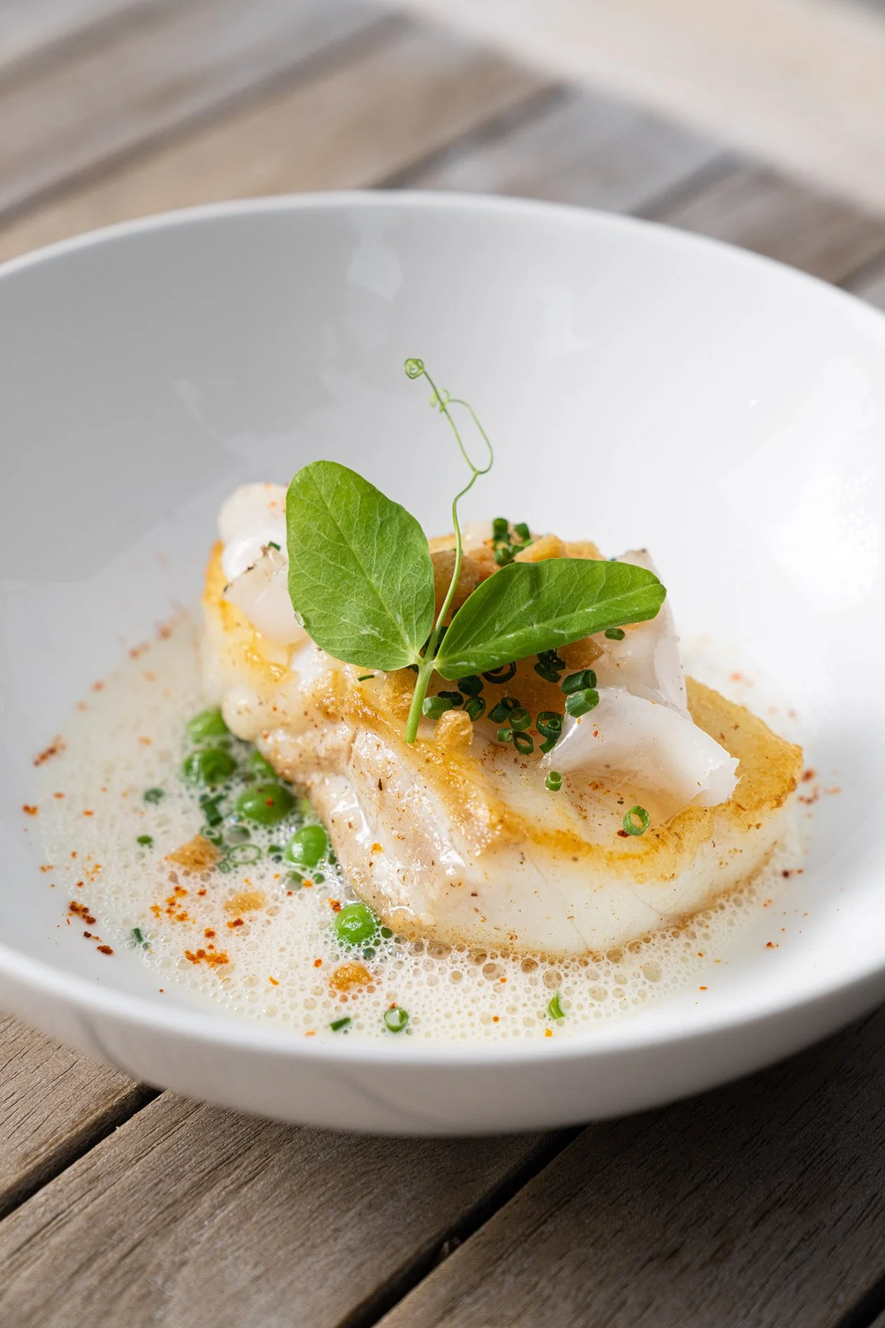 Gourmetgericht mit Fischfilet, Erbsen und Schaumsoße, garniert mit frischen Kräutern in einer weißen Schüssel.