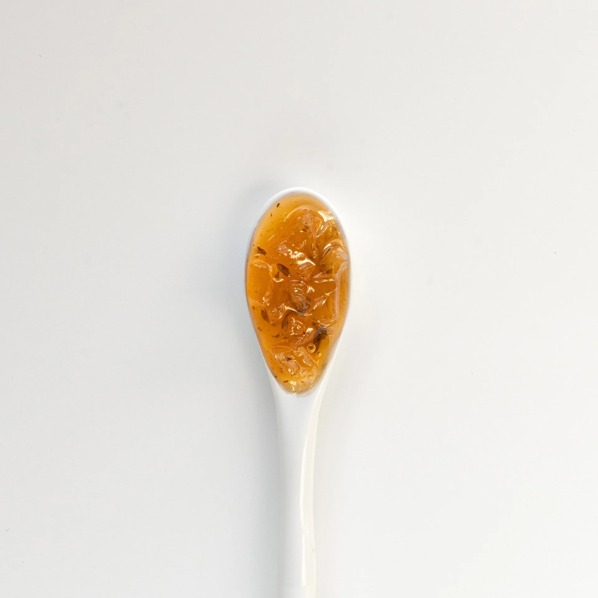 Ein Löffel mit gelblichem Gelee oder Marmelade auf weißem Hintergrund.