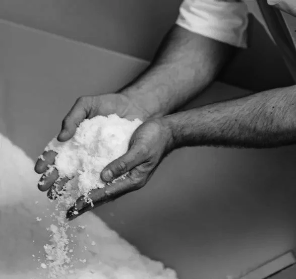 Person, die Salz zwischen den Händen hält über einem großen Behälter.