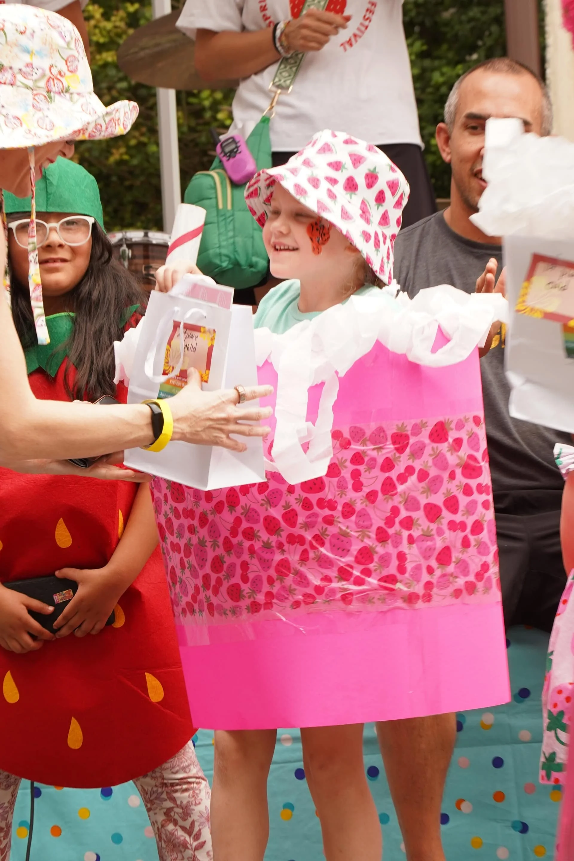 Children receiving prizes during a strawberry-themed costume activity at an outdoor festival.