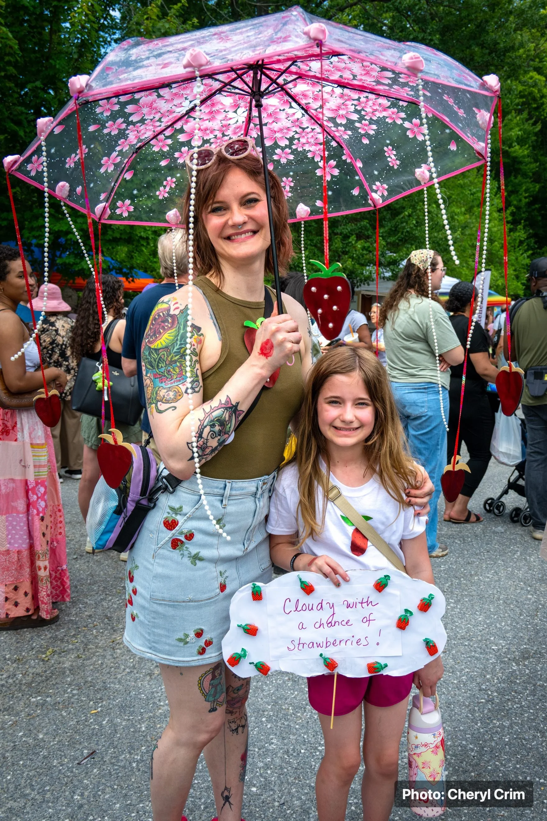 An adult and child posing together at the Strawberry Festival with a strawberry-themed umbrella.