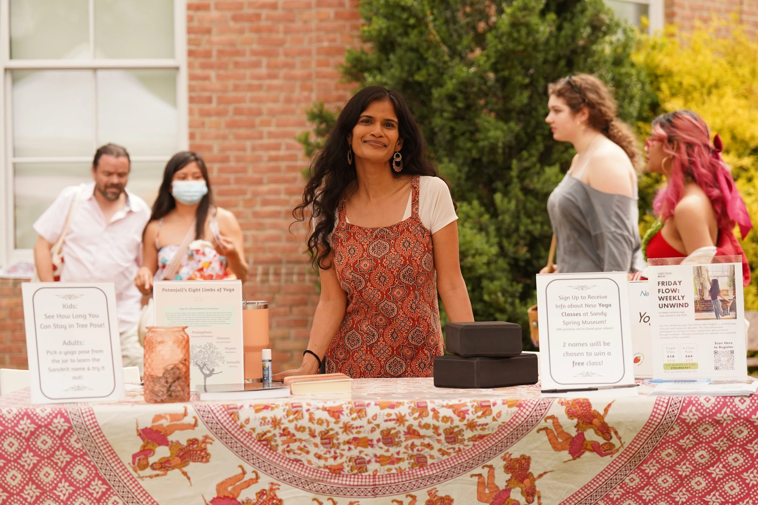 Neha Singhal at a Friday Flow yoga information table outdoors at Sandy Spring Museum