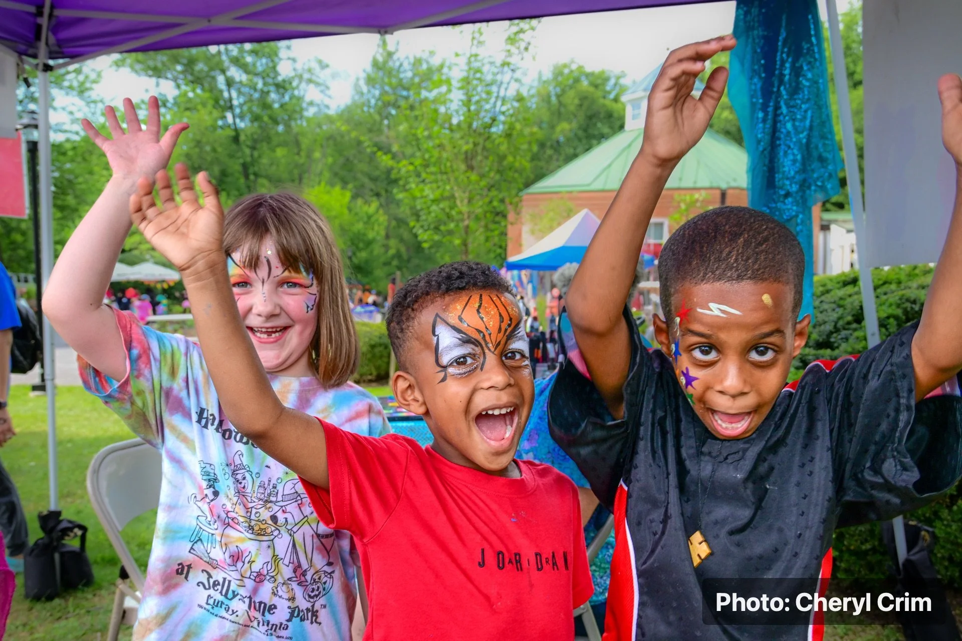 Children raising their hands during an outdoor Strawberry Festival activity.