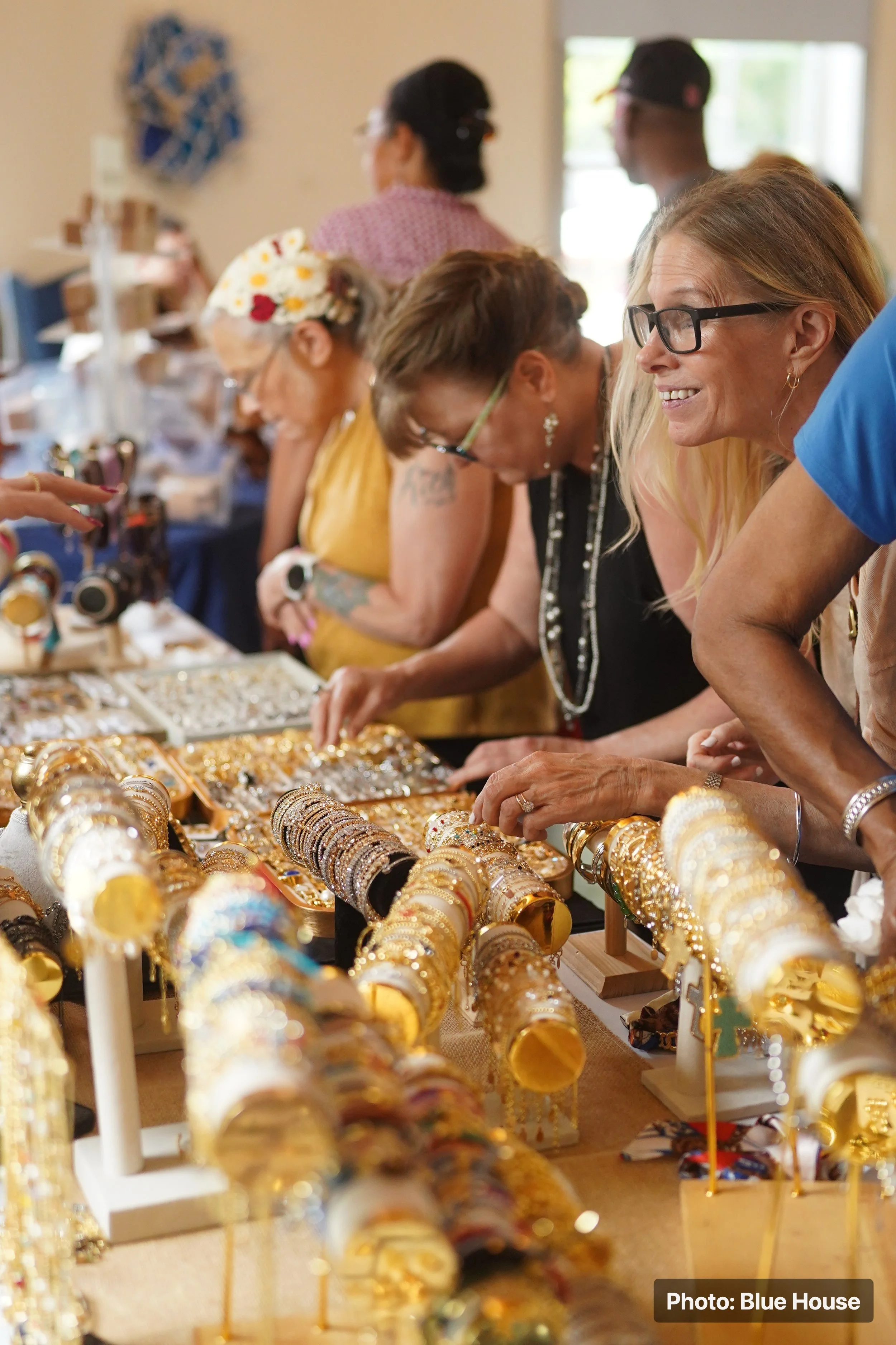 People shopping for jewelry at a market stall filled with gold bracelets and rings.
