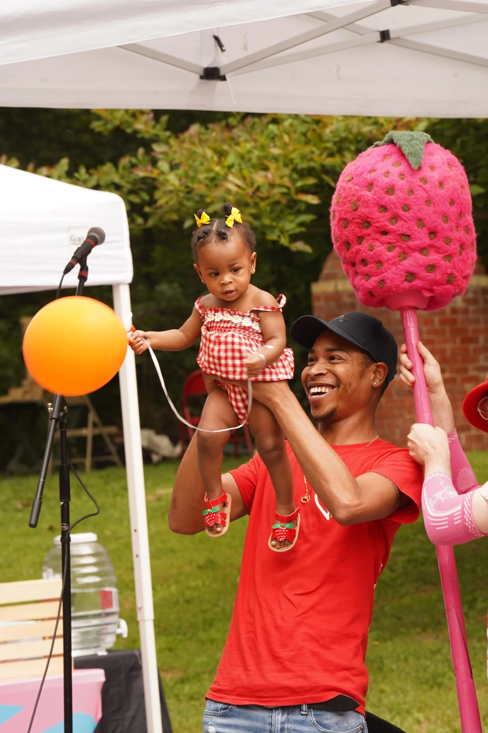 A child being lifted near a stage during a strawberry-themed festival activity.