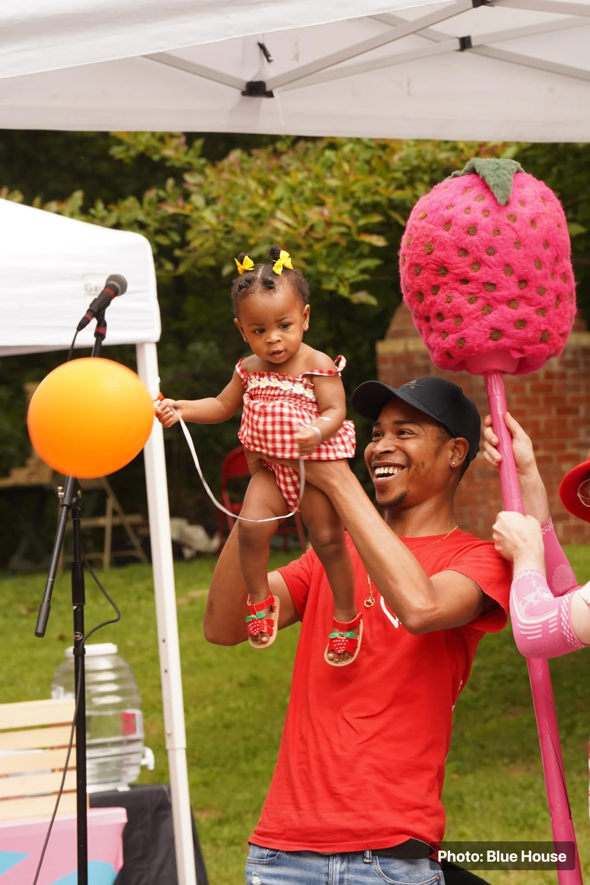 A child being lifted near a stage during a strawberry-themed festival activity.