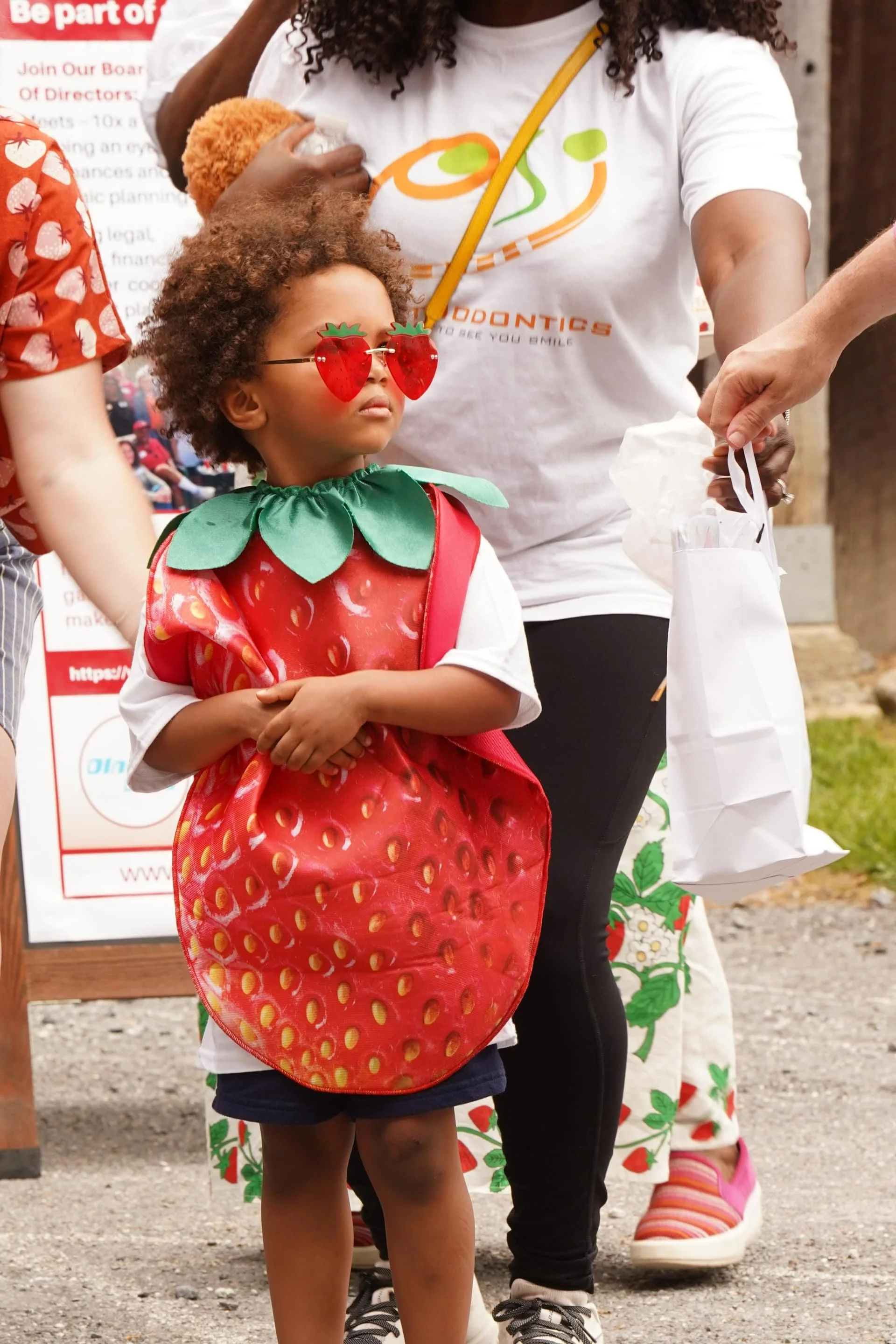 A child wearing a strawberry costume and sunglasses during a community festival activity.