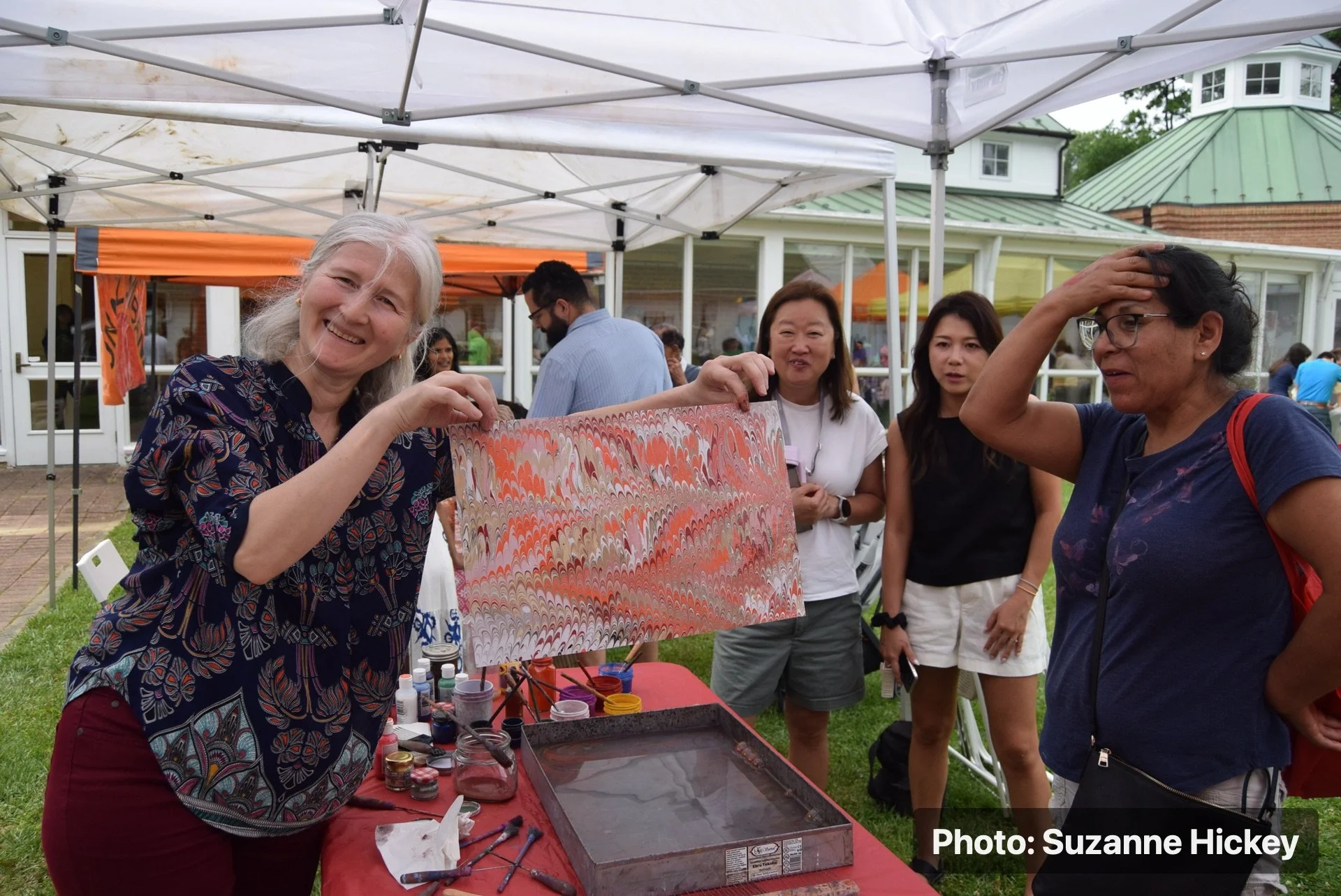 A person demonstrating a colorful printed cloth at a Strawberry Festival vendor tent.